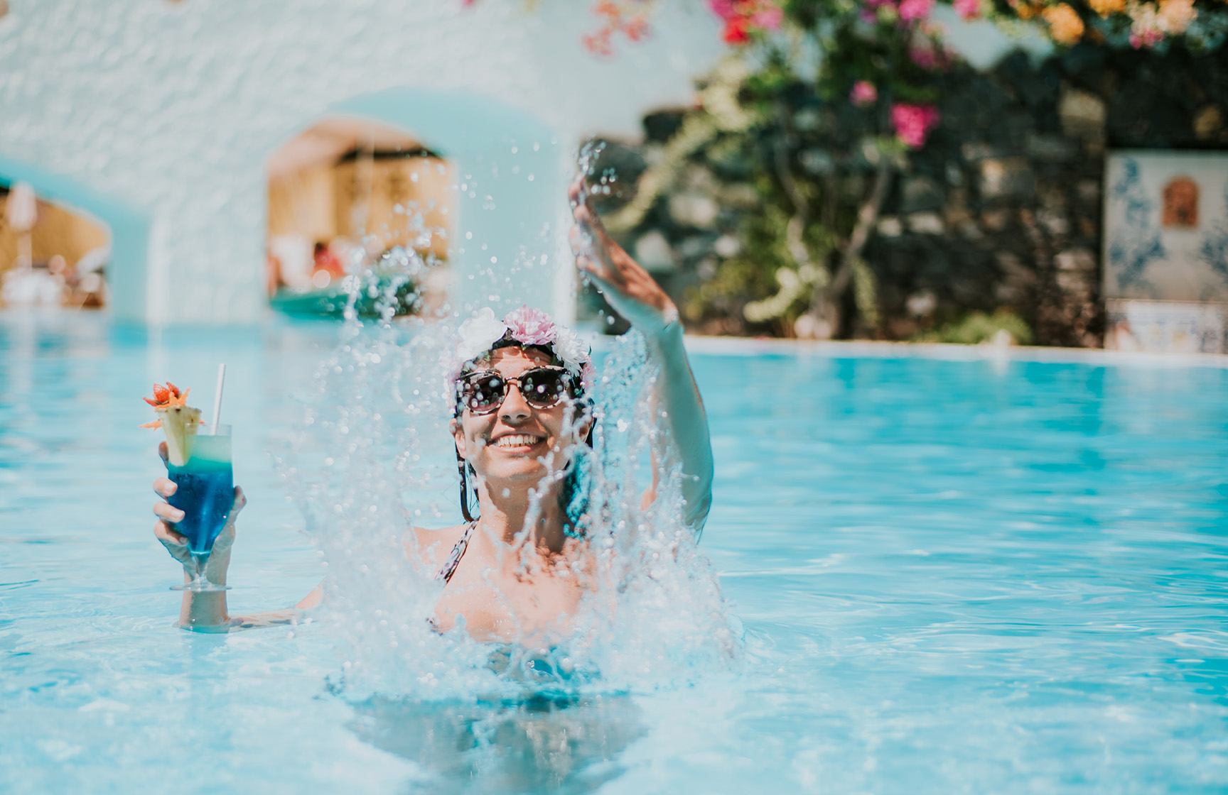 Happy woman playing with water, holding a cocktail, enjoying the all-inclusive package without worries