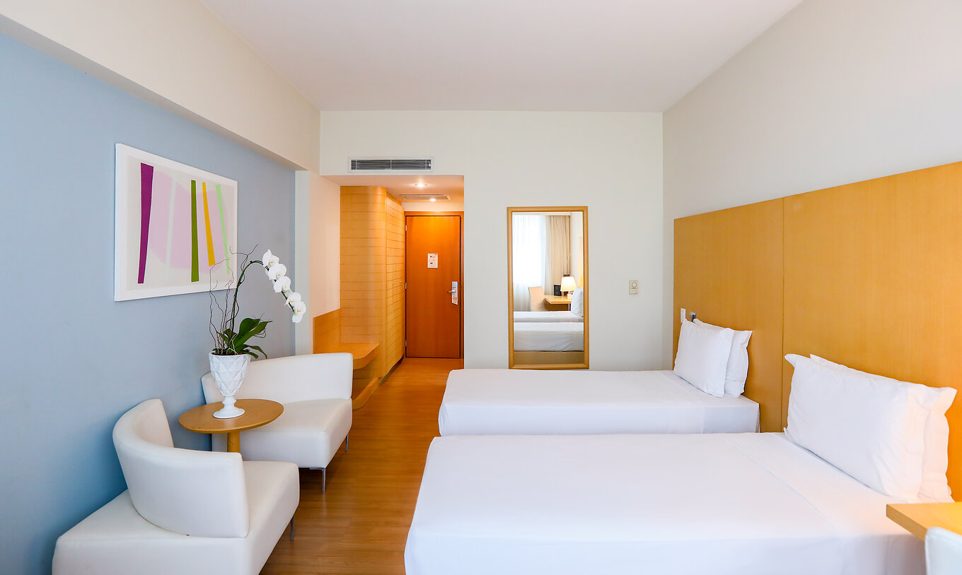The Twin Superior at Pestana Curitiba has two single beds with sofas at the foot of the bed and a small table with flowers