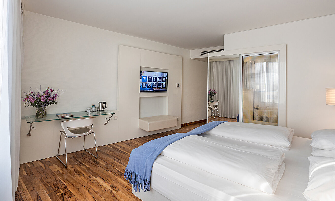 Deluxe room at Pestana Berlin Tiergarten has a TV, a desk with lamp and chair, sofa and armchair