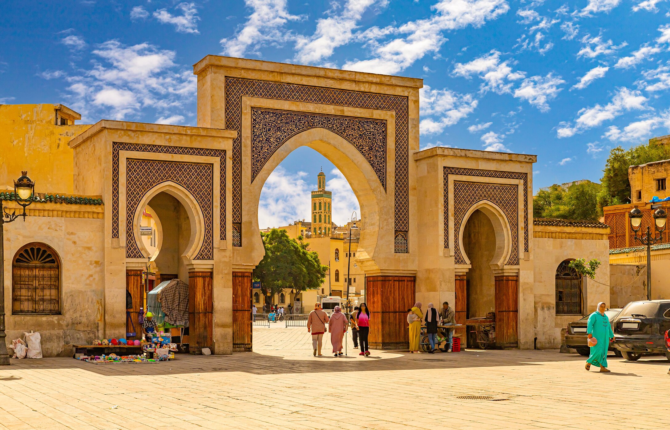 Typical Moroccan arches in Fez, with sand-colored tiles, and people walking in traditional clothes.