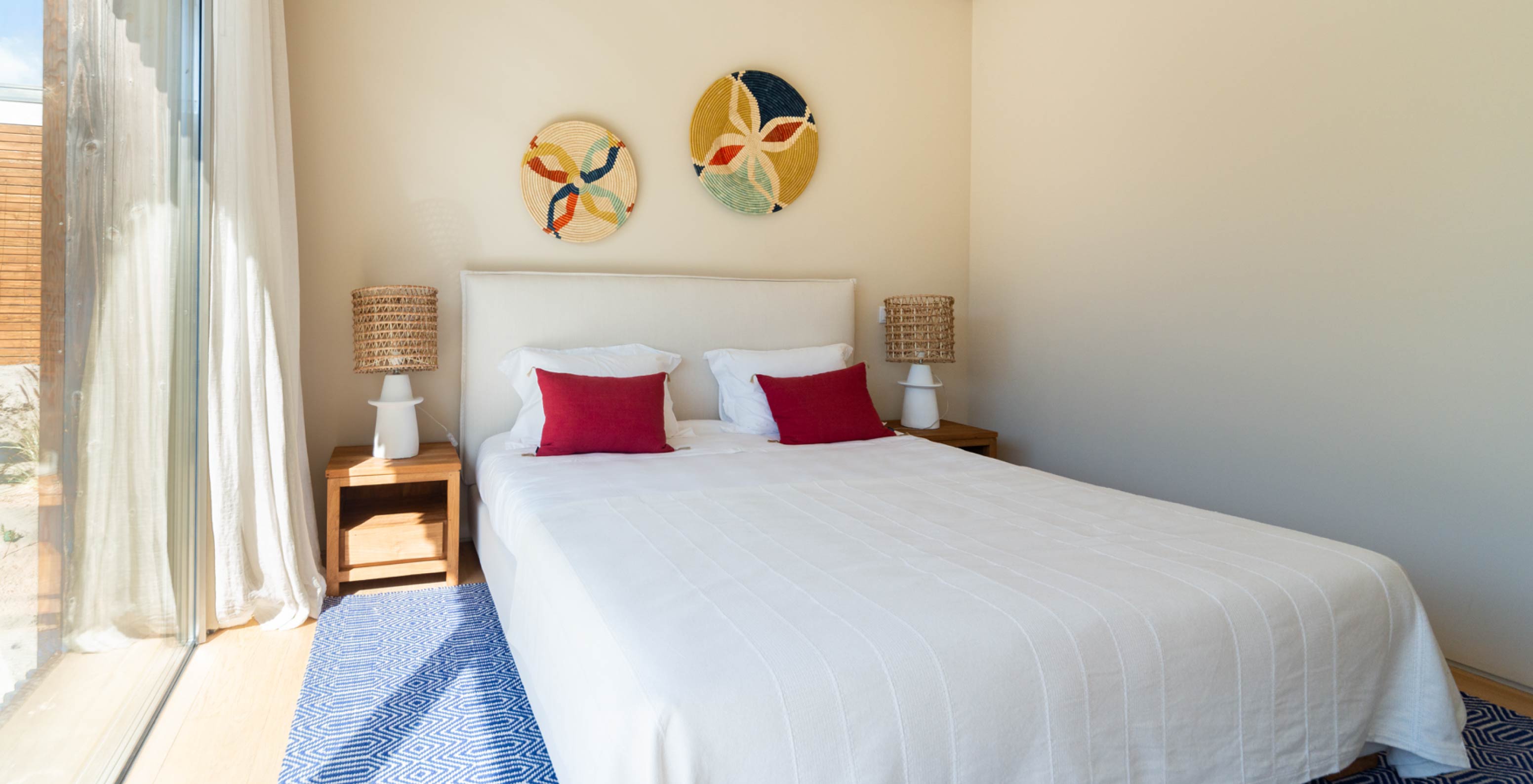 The exclusive villa with a pool at Pestana Tróia Eco Resort has a bedroom with a double bed, red cushions, and a blue rug