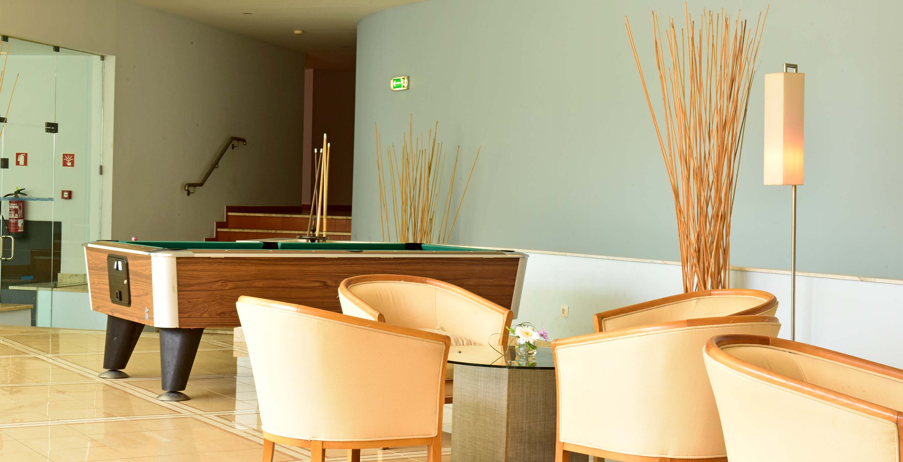 Game room with a snooker table, chairs, and central support table with stairs in the background and decoration