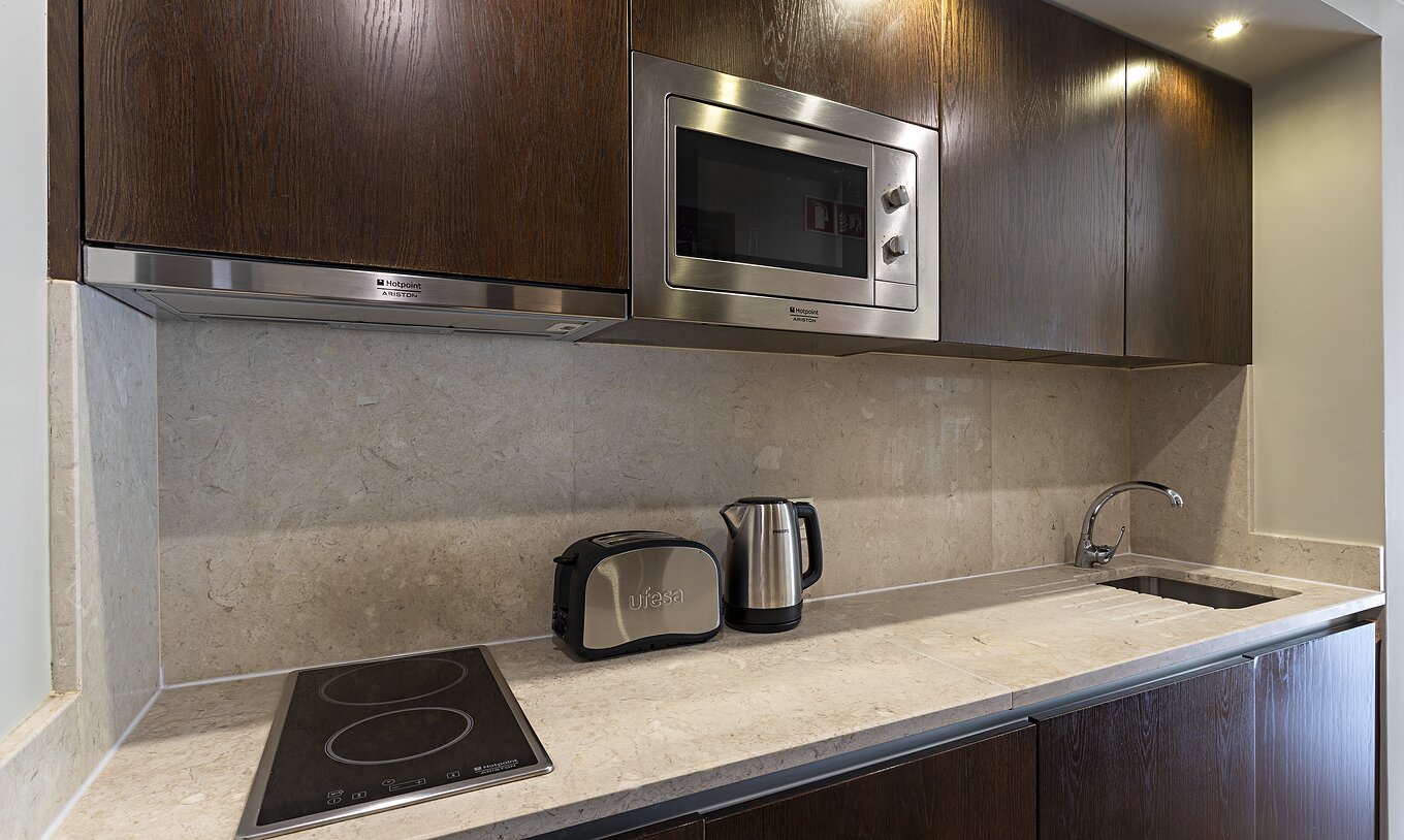 The Cliff Studio at Pestana Alvor Praia has a dark wood kitchen and a stone countertop, with a stove and a microwave