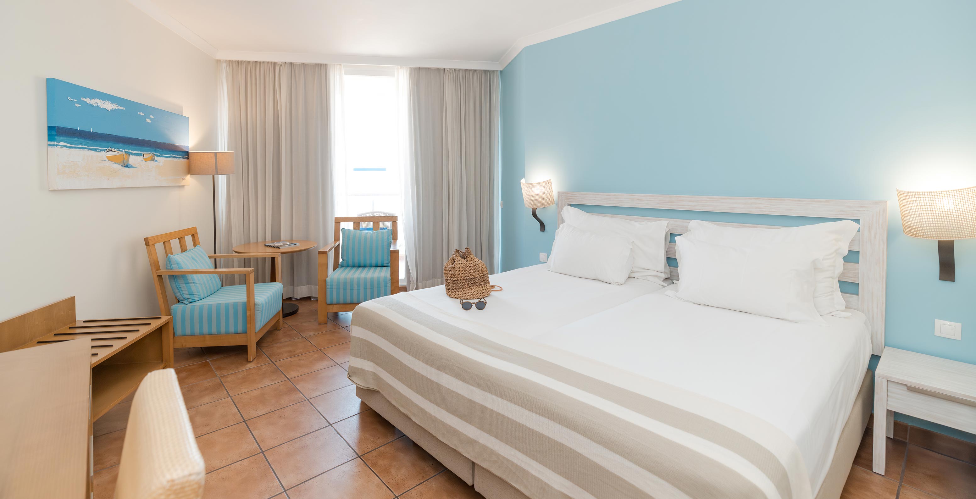 The Deluxe Side Sea View at Pestana Viking has two beds, bedside table and two armchairs by the window