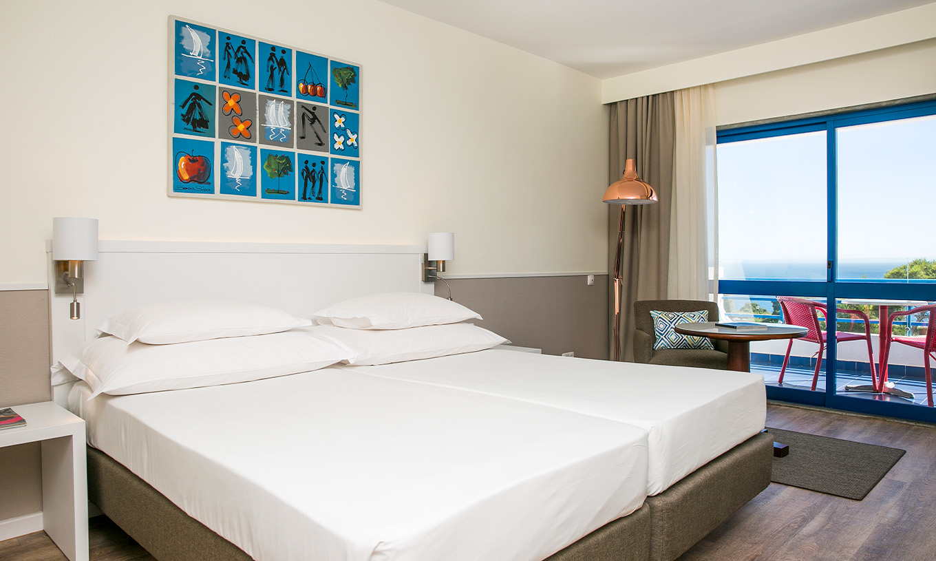 The Deluxe Sea View room at Pestana Cascais has two single beds, bedside lamps, and an armchair with a table