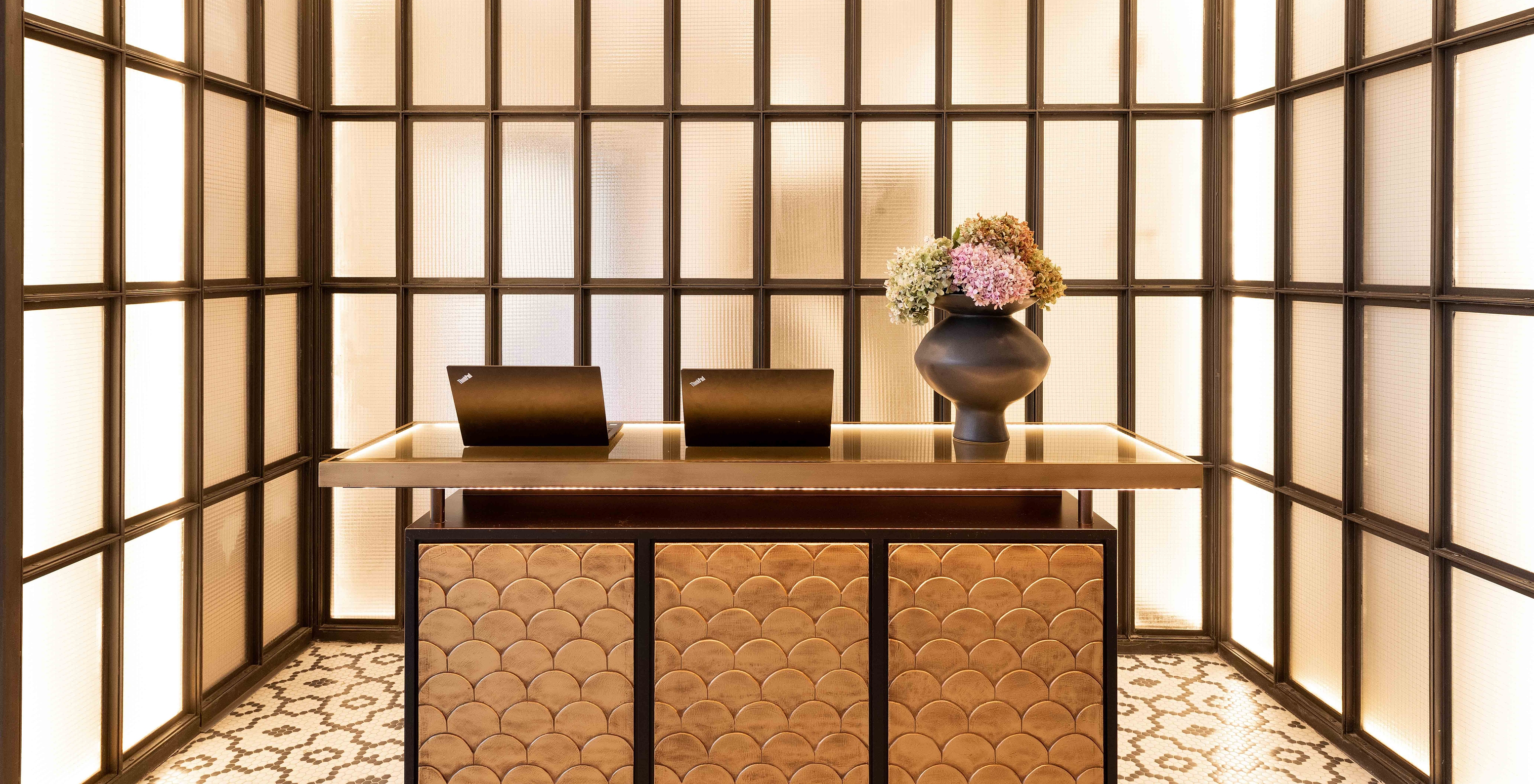 Reception desk with two laptops, a vase with flowers and a wall with illuminated rectangles