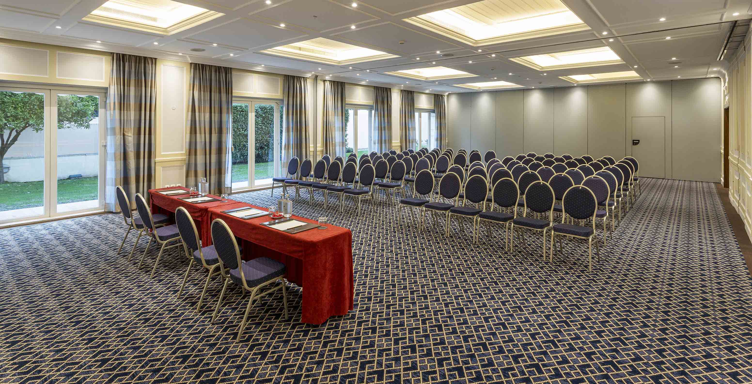 Pestana Palace Lisboa has a large meeting room with blue chairs, tables, and big windows overlooking the garden