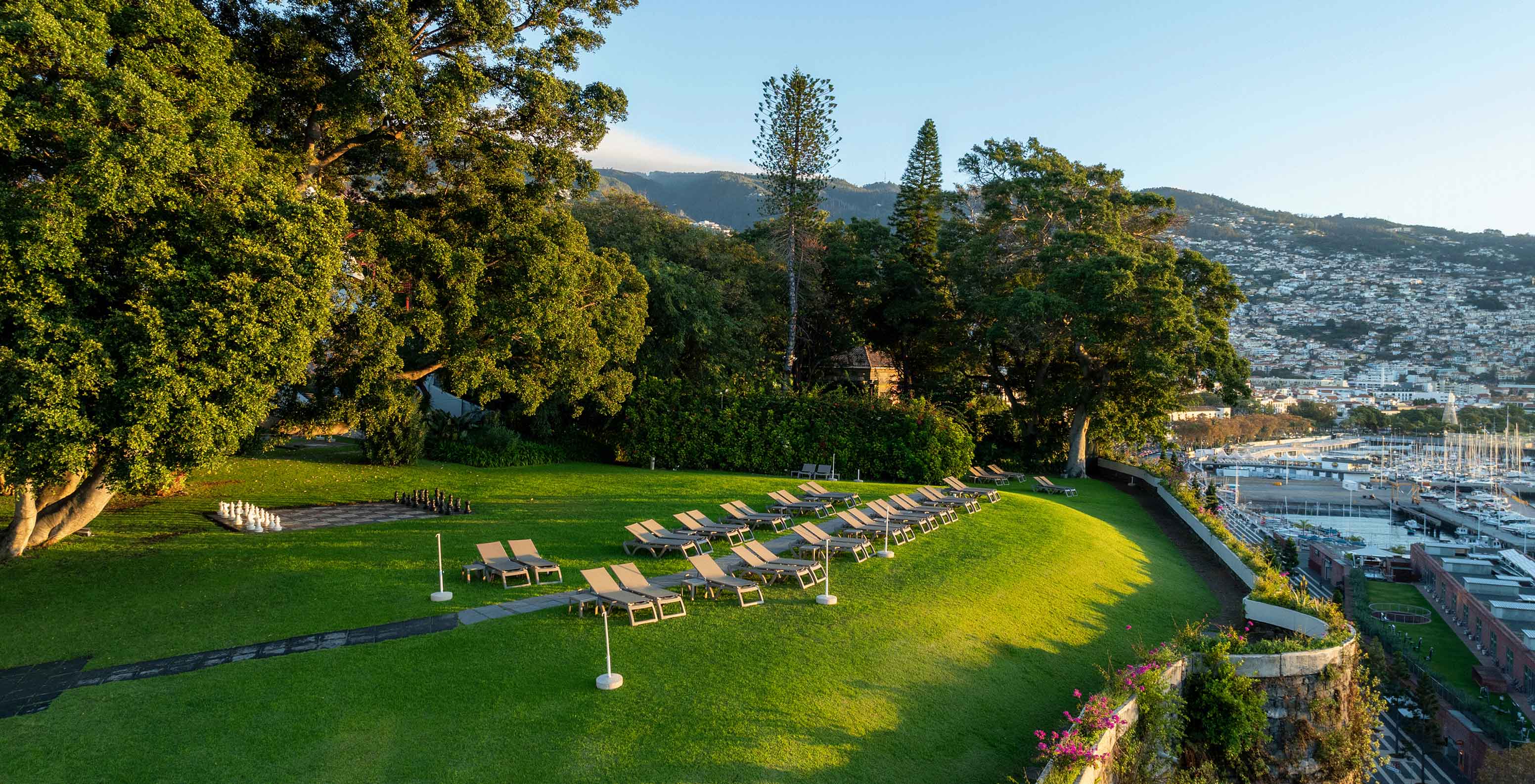 View of the Pestana Casino Park garden at sunset, with a city in the background and a cruise ship anchored at sea