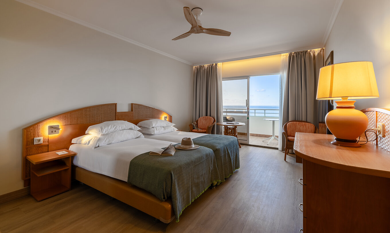 The Pestana Ocean Bay All Inclusive Classic Sea View has a double bed, a TV cabinet, two chairs, and a balcony with a view
