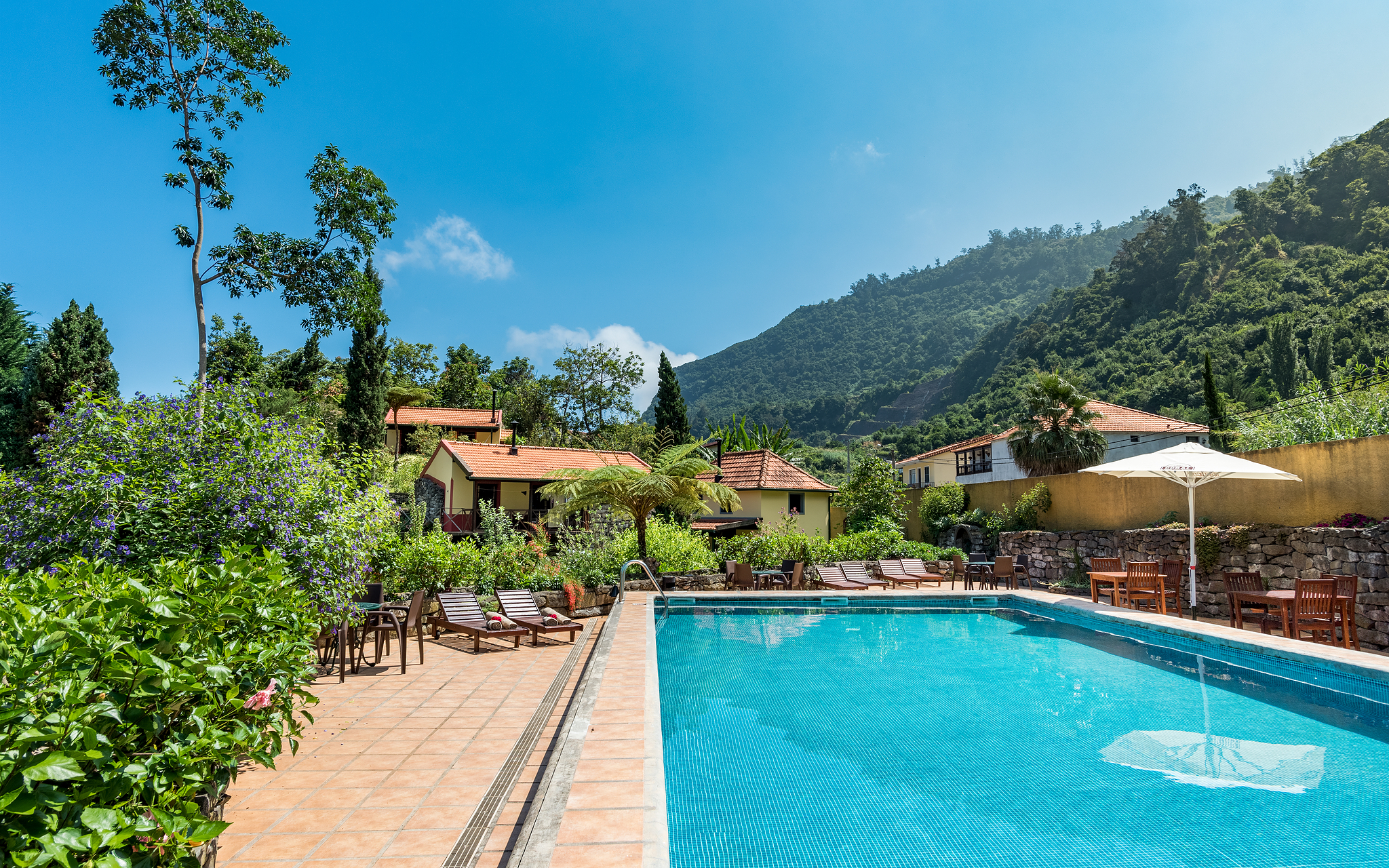 Pool of Pestana Quinta do Arco, a rural tourism hotel in Madeira, with sun loungers, vegetation, villas, and mountains