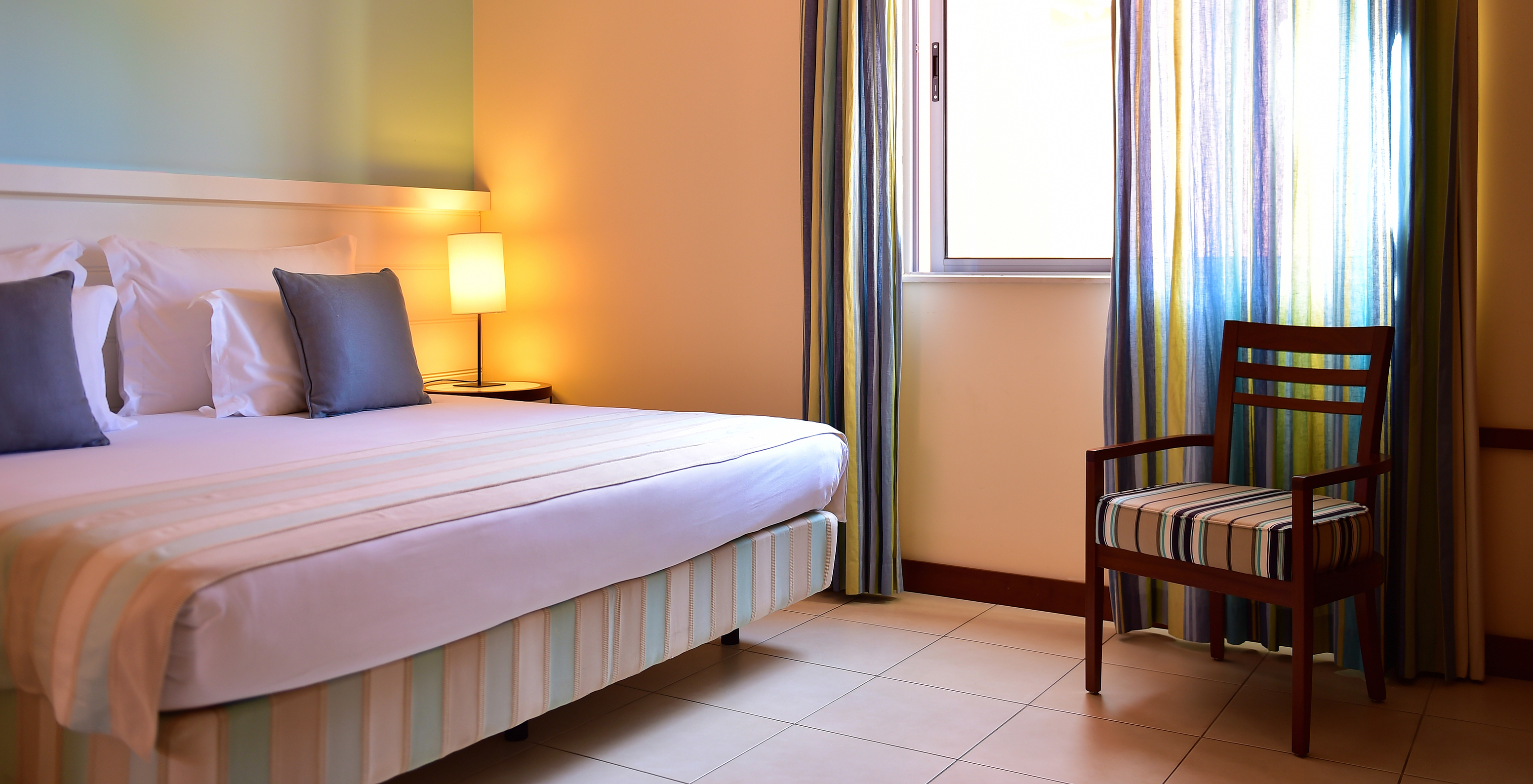 The T2 Suite Apartment of Pestana Porto Santo All Inclusive has a bedroom with a double bed, a chair, and a window