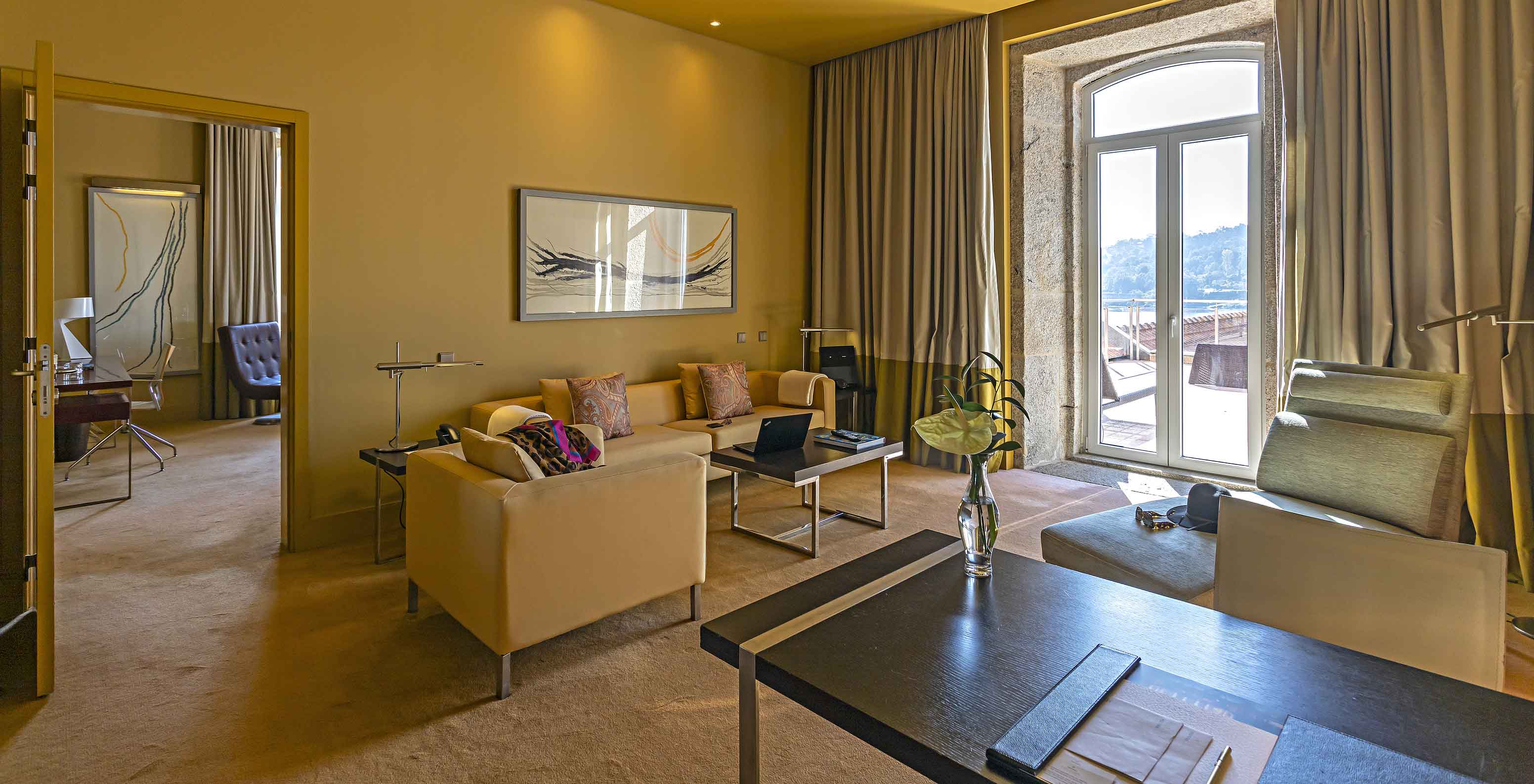 The Suite Nasoni has a living room with sofas, a desk, and a stone-framed window to the balcony