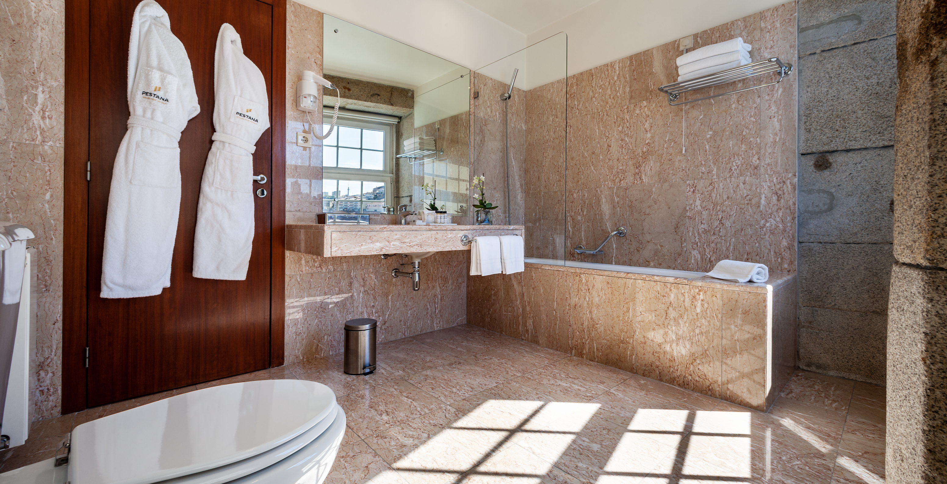The Plaza room at Pestana Vintage Porto has a bathroom with bathtub, two bathrobes, sink and hairdryer