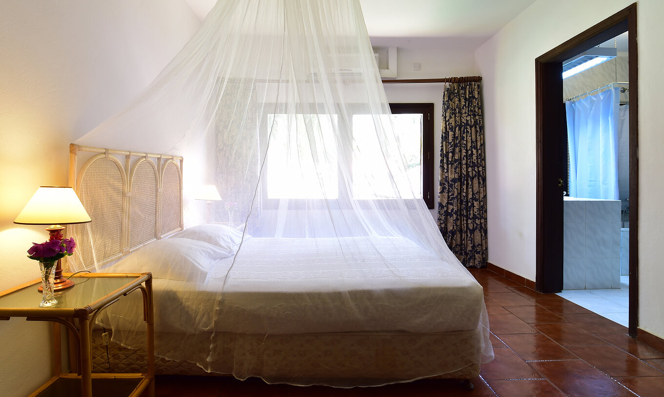 The Suite at Pestana Miramar São Tomé includes a double bed with a mosquito net, a bedside table, and a window