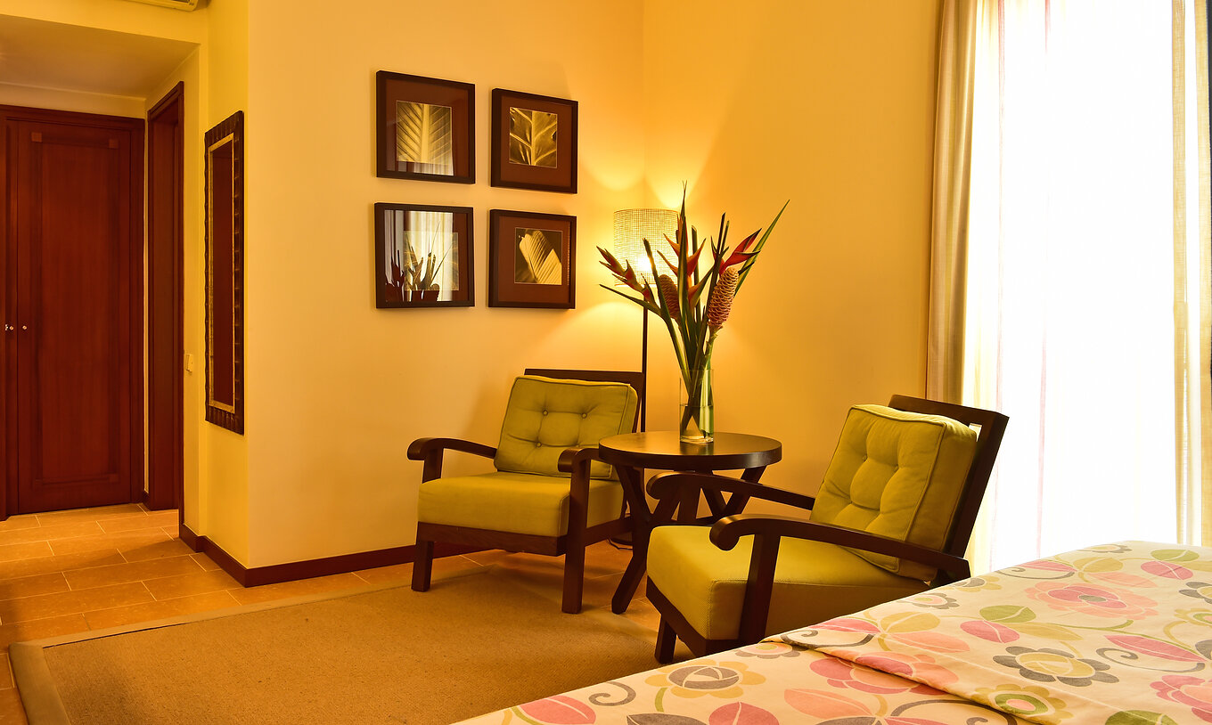 The Junior Suite of Pestana São Tomé has two armchairs at the foot of the bed with a small table and a vase of flowers