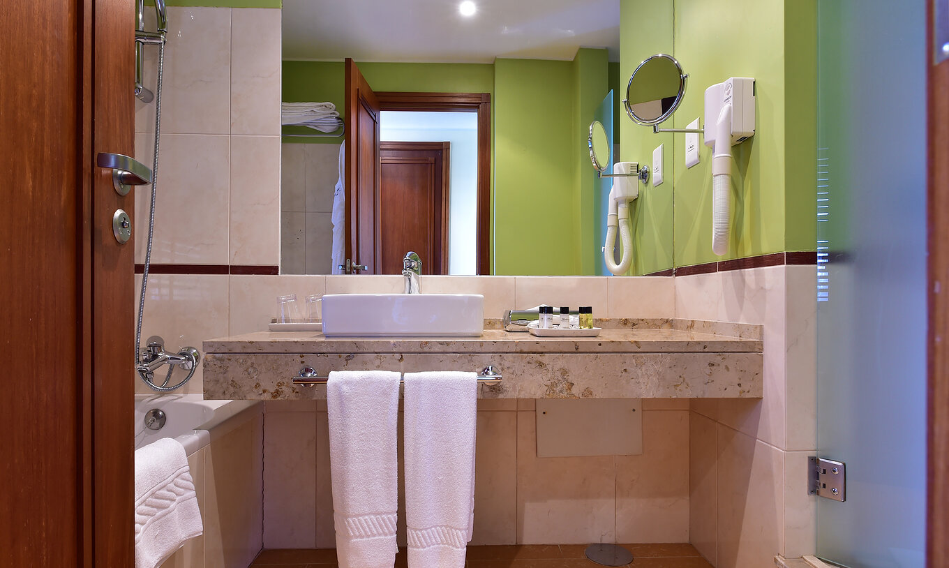 The Sea View Room of Pestana São Tomé has a bathroom with bathtub with shower and a neutral and green decor