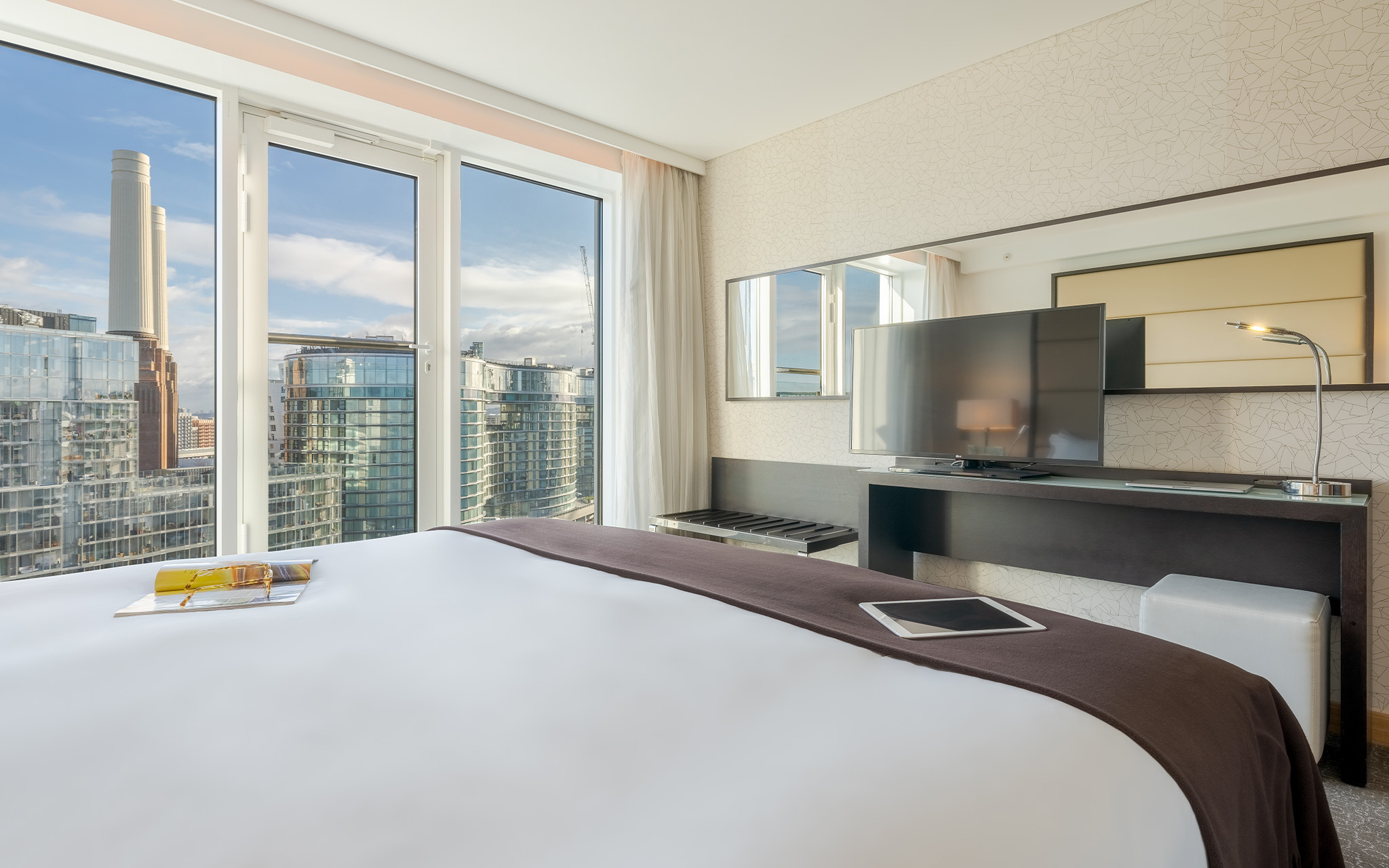 Room with a double bed, television, mirror, and large windows overlooking the city of London