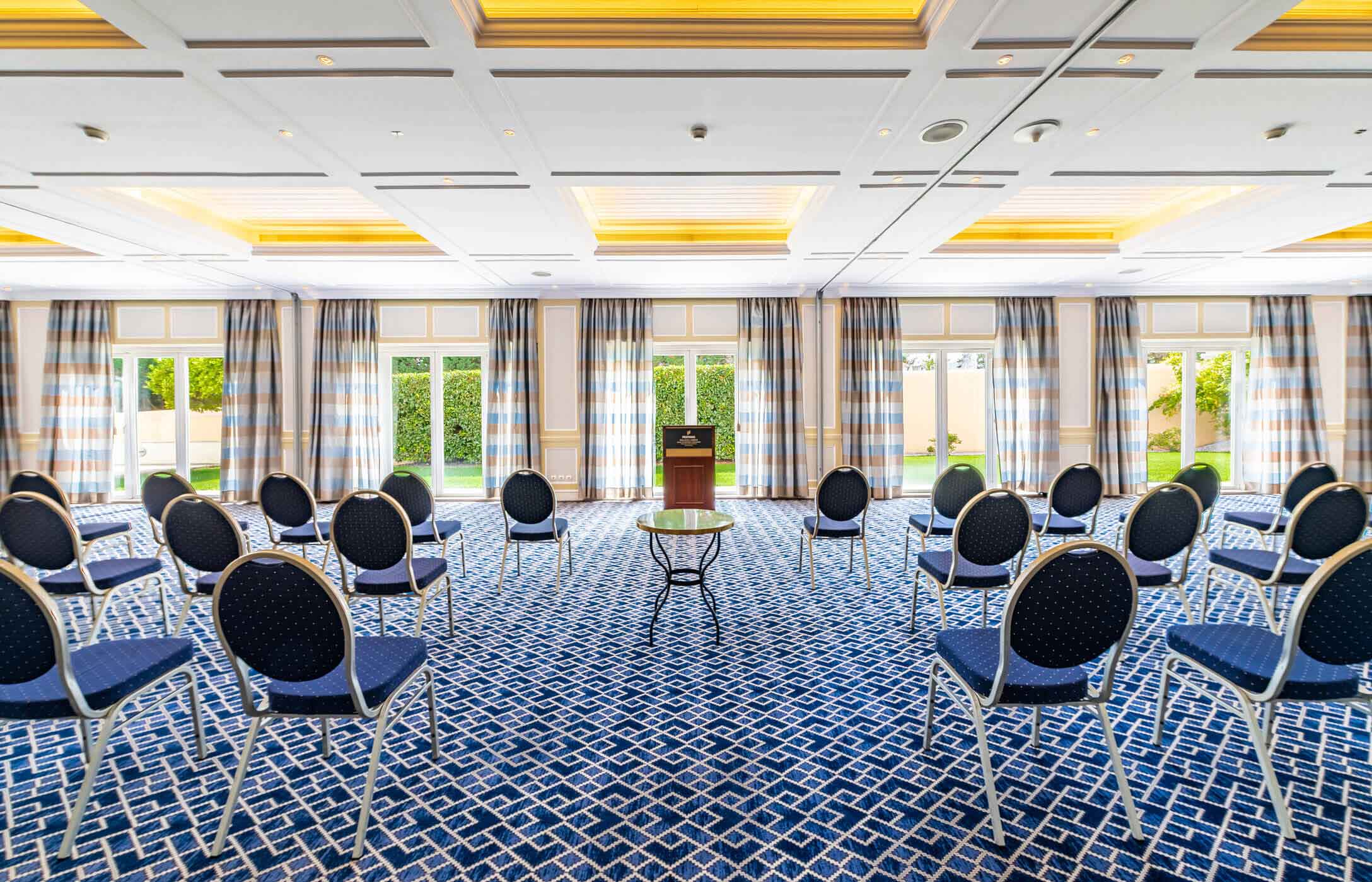 Meeting or conference room, with soft lighting, blue geometric pattern carpet, multiple chairs, and a podium