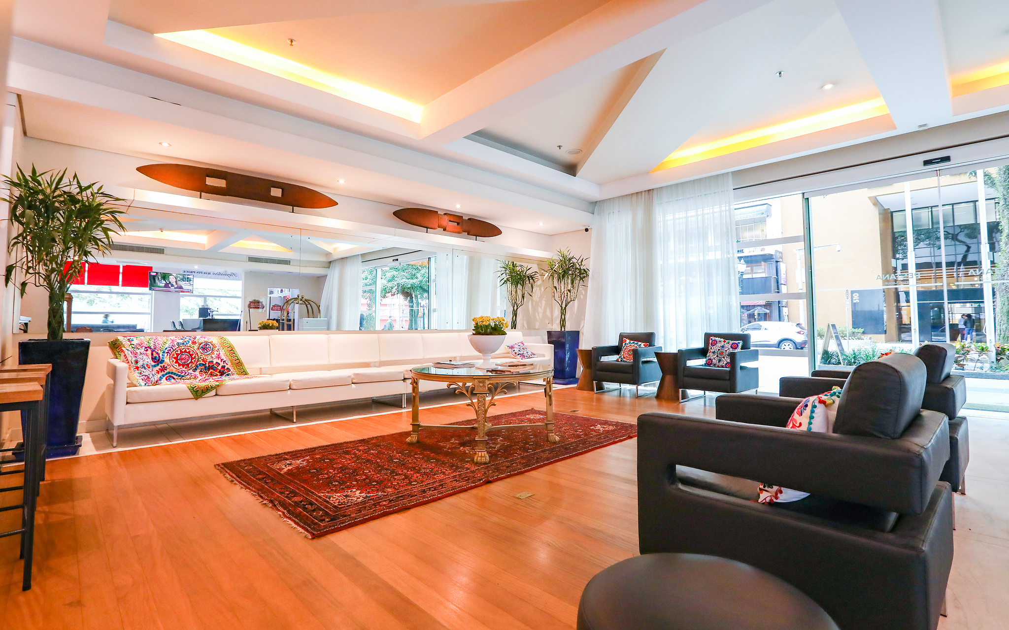 Entrada de Pestana Curitiba con 4 sillones y sofá blanco largo con almohadas coloridas y mesa de centro