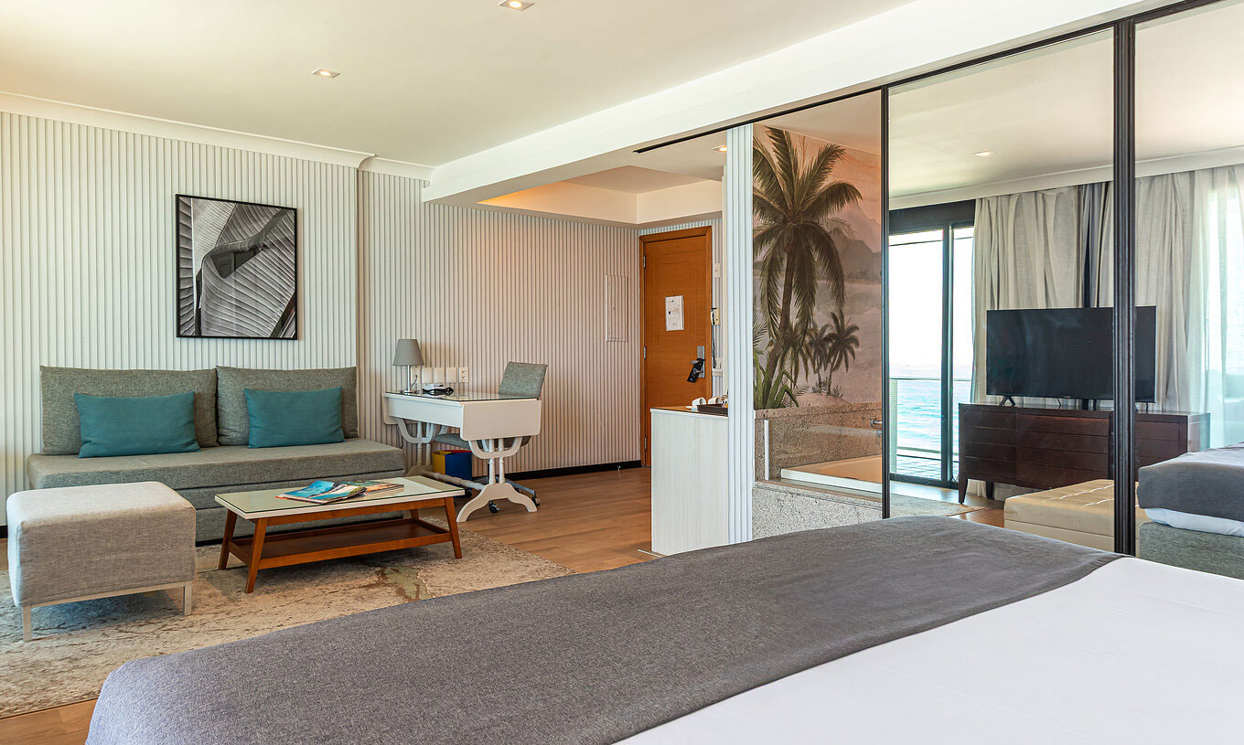 La Suite Oceánica del Pestana Rio Atlântica tiene cuarto moderno con cama, sofá, mesa y TV.