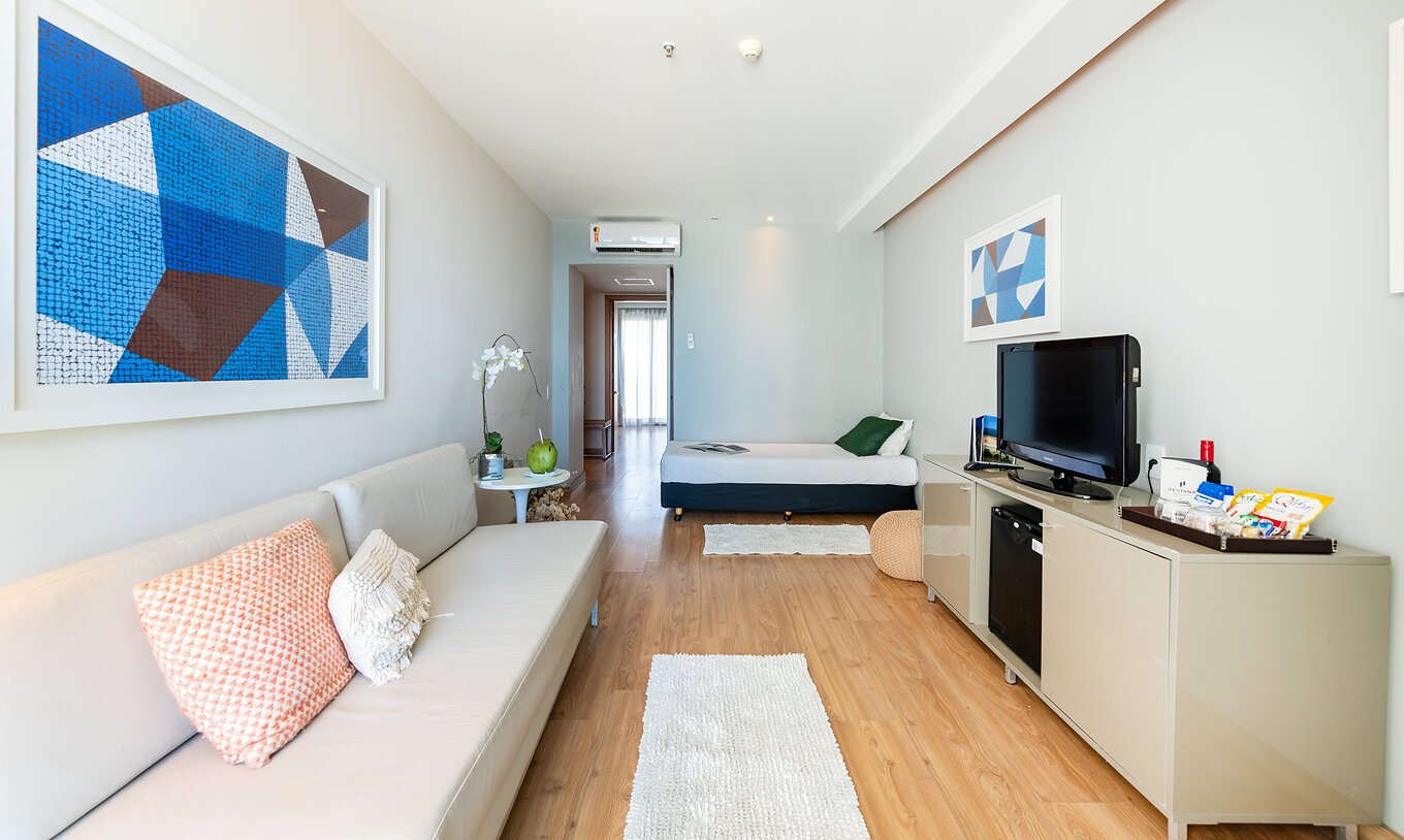 La Suite Vista Mar Lateral del Pestana Rio Atlântica tiene una sala con sofá, cama, una televisión y un cuadro azul