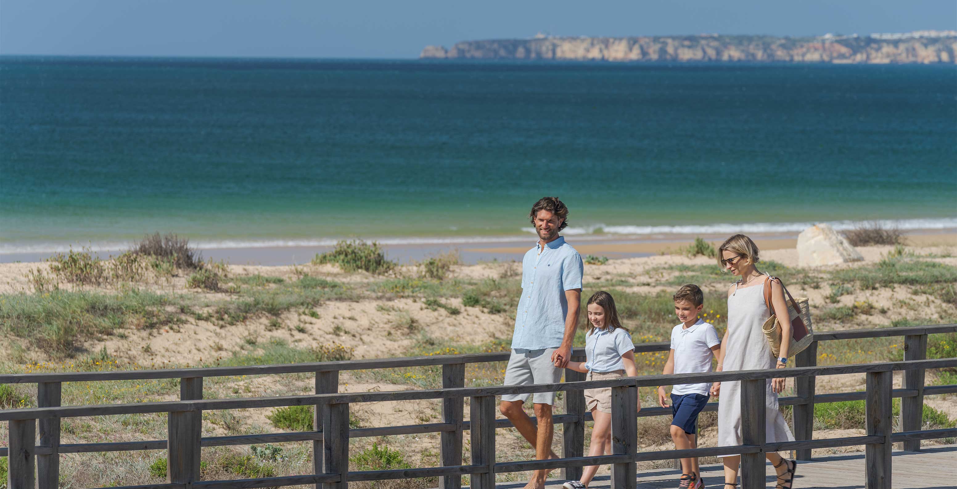 Familia pasea sonriente, en el paseo junto a la playa de Alvor, en el Algarve