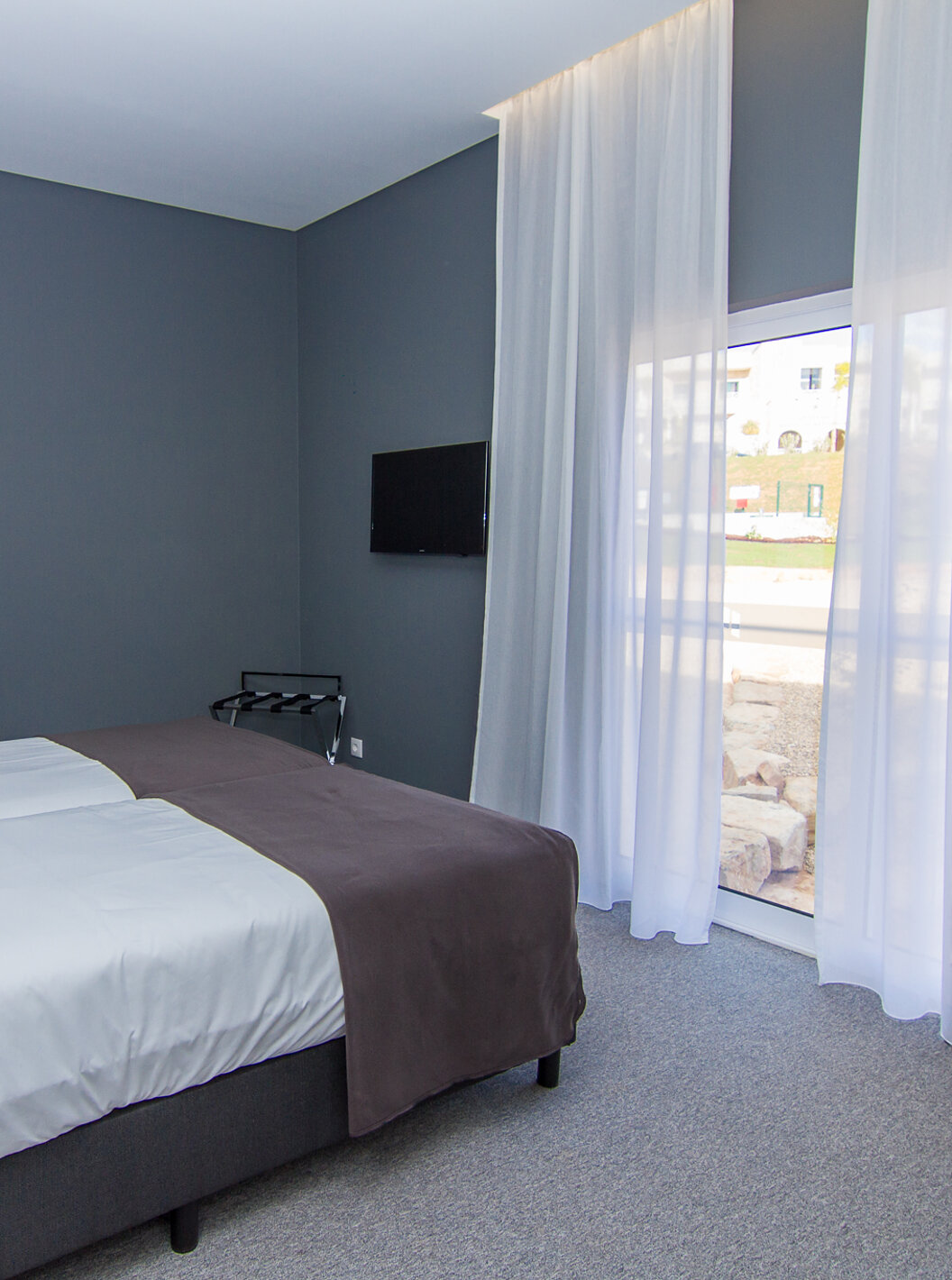 El Cuarto Clásico del Pestana Gramacho Residences tiene dos camas individuales, un televisor y una ventana con cortinas