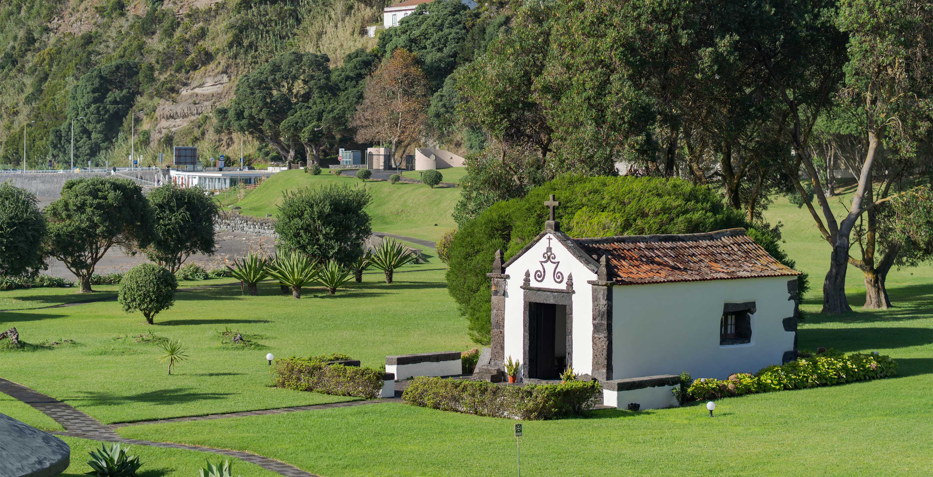 Capilla en el exterior del hotel, en medio de jardines verdes con árboles y pequeños paseos para los clientes