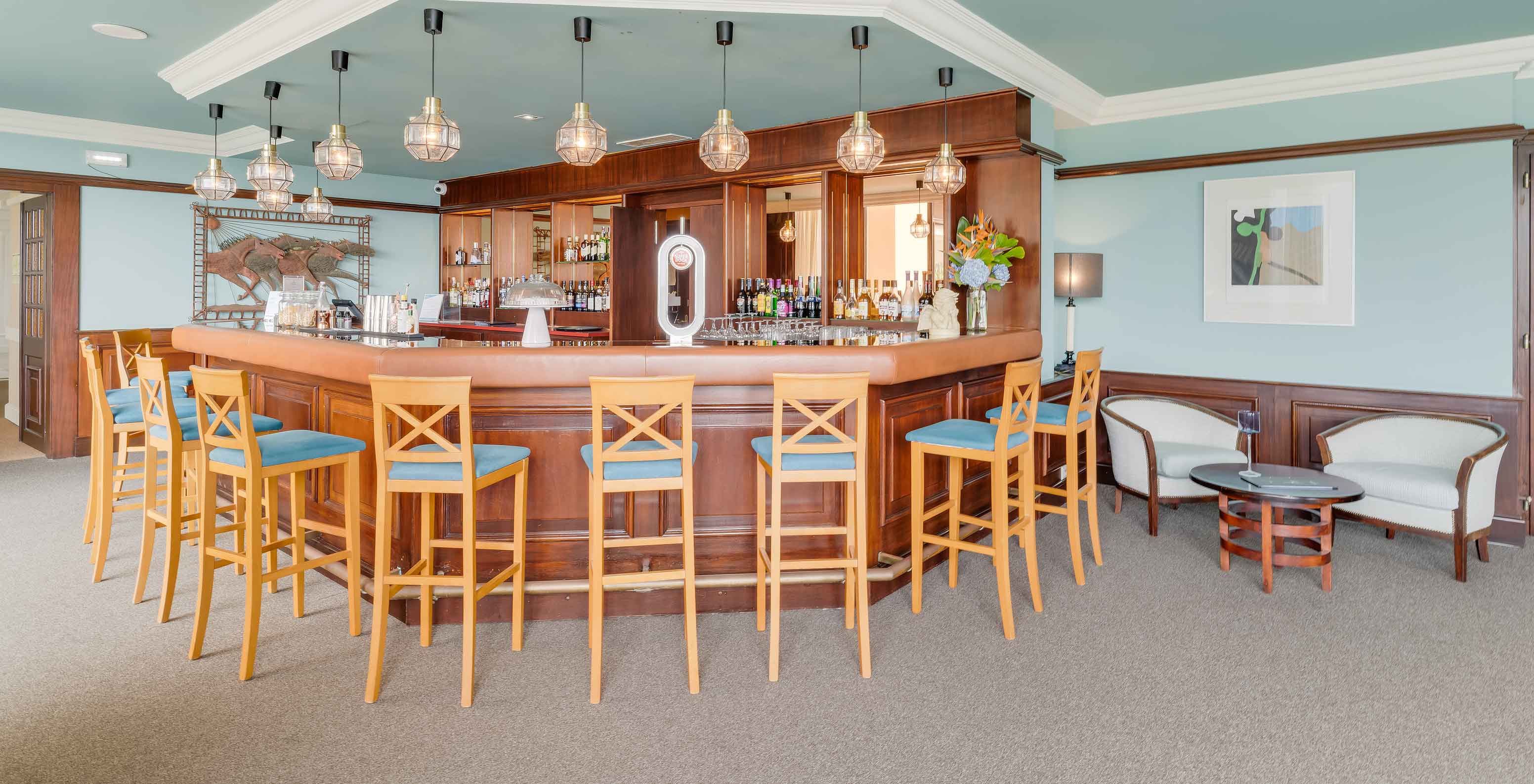 Bar en Pestana Bahia Praia con taburetes altos, barra de madera y iluminación moderna con bombillas colgantes