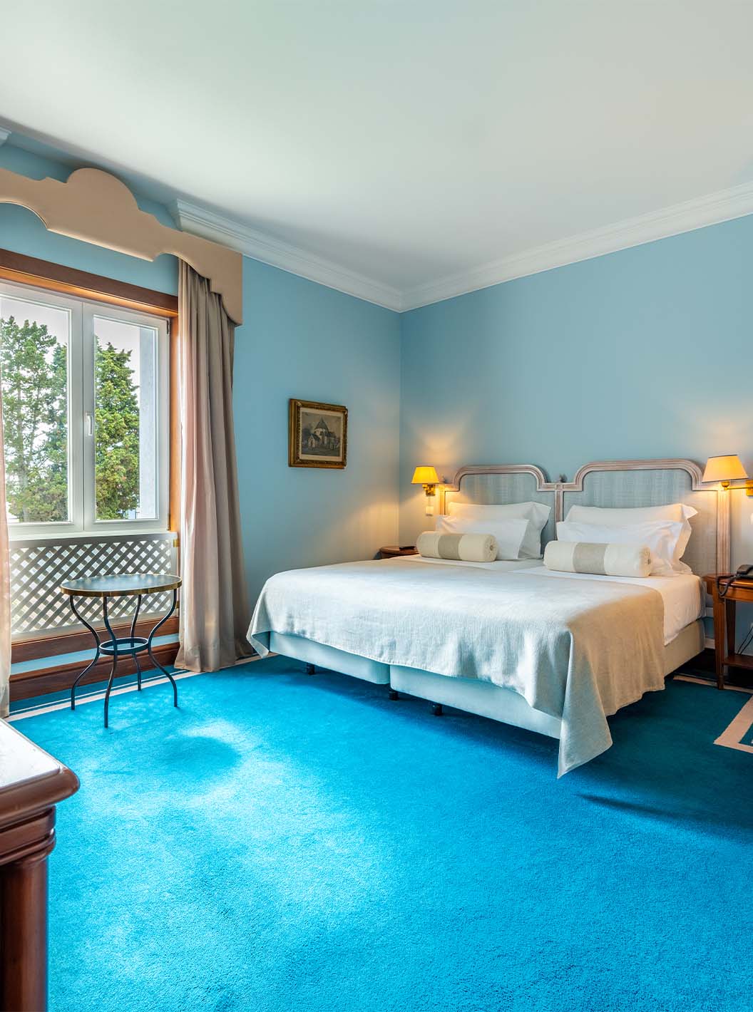 El Deluxe del Pestana Palace Lisboa tiene dos camas individuales, una ventana, sillón, escritorio y una alfombra azul