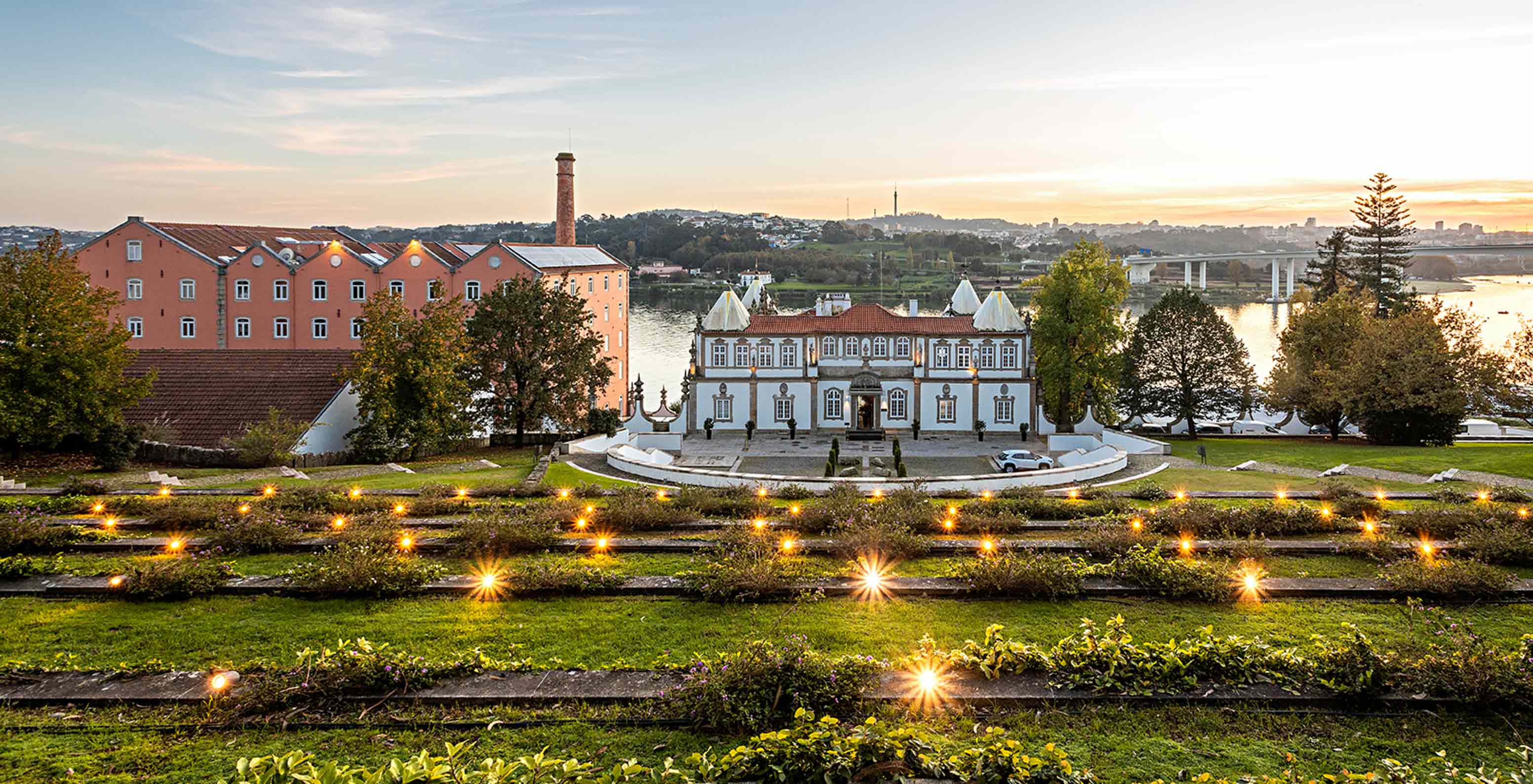 Vista exterior de la fachada del Pestana Palácio do Freixo rodeado de jardines con vistas al río Duero al atardecer
