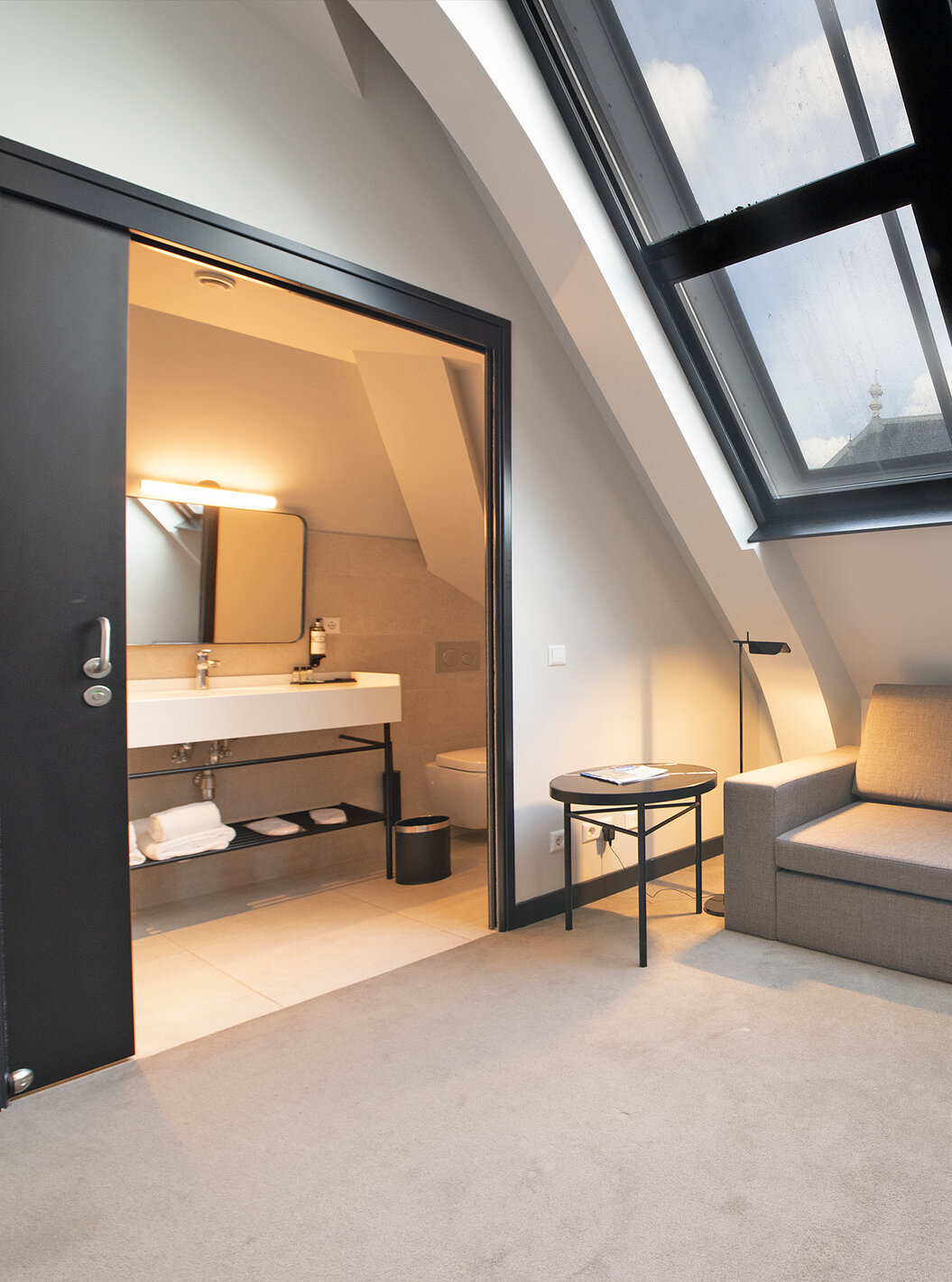 El cuarto Loft del Pestana Amsterdam Riverside tiene un sofá gris y un baño con lavabo y espejo