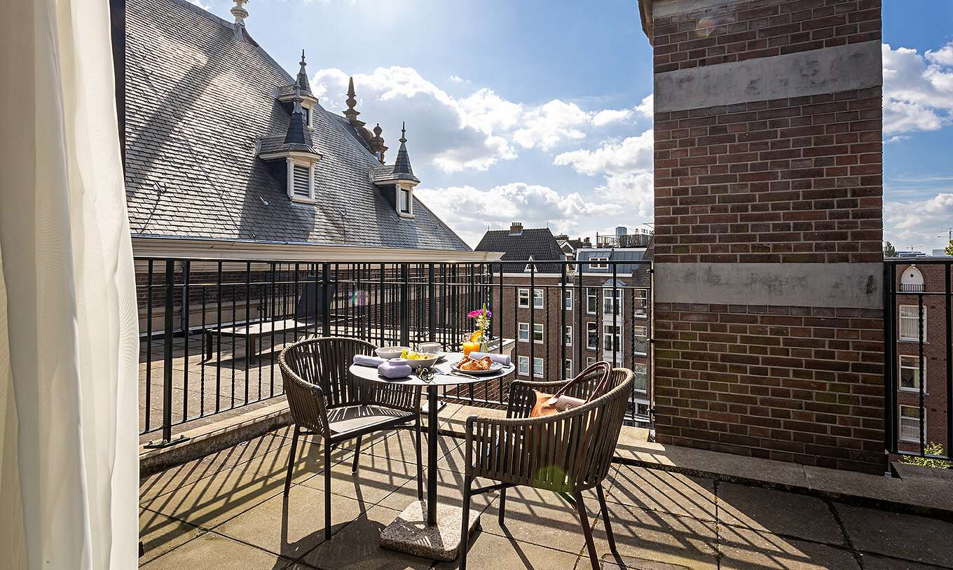 El cuarto Executive Terrace del Pestana Amsterdam Riverside tiene un balcón con una mesa con comida y dos sillas