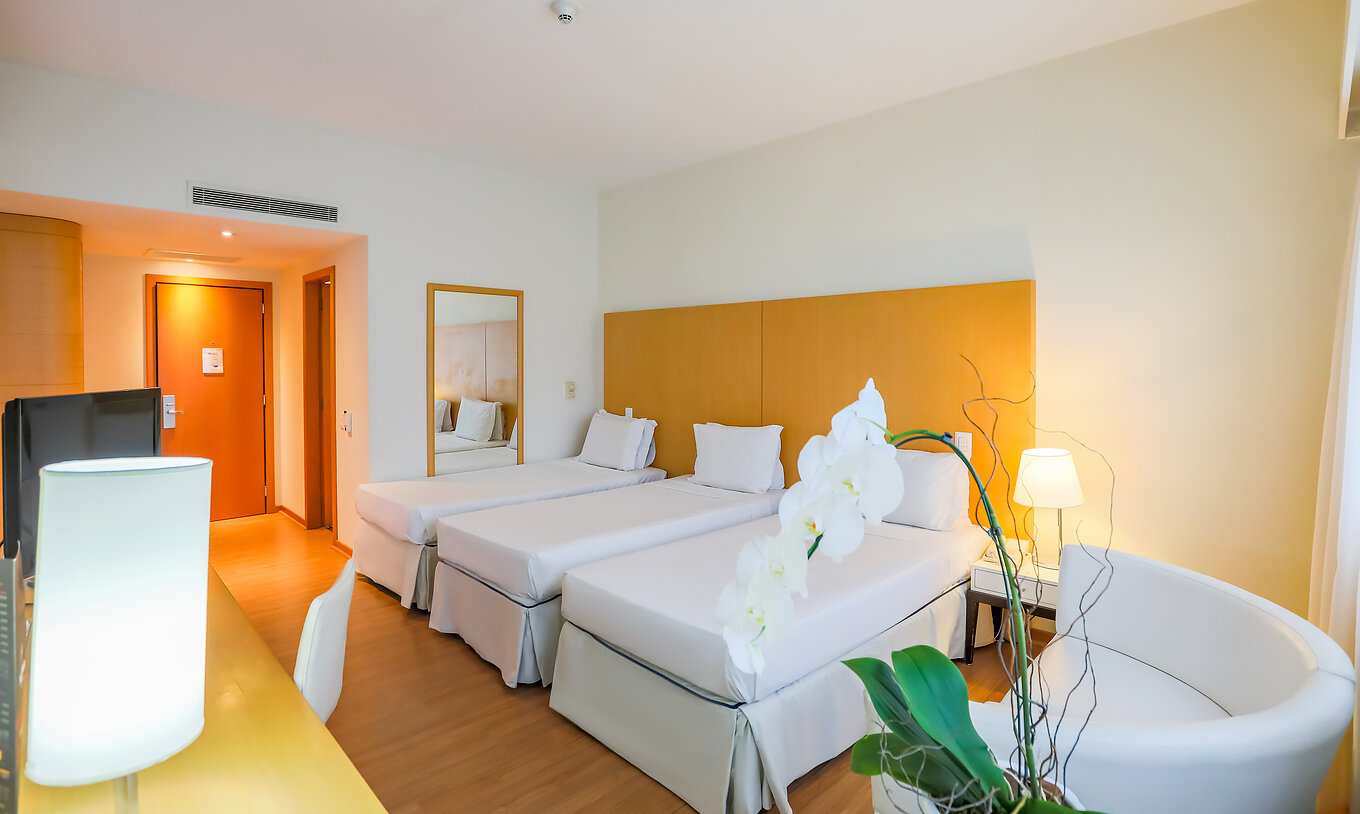 El Twin Luxo Corner del Pestana Curitiba tiene tres camas individuales con una mesa con televisión y un pequeño sofá