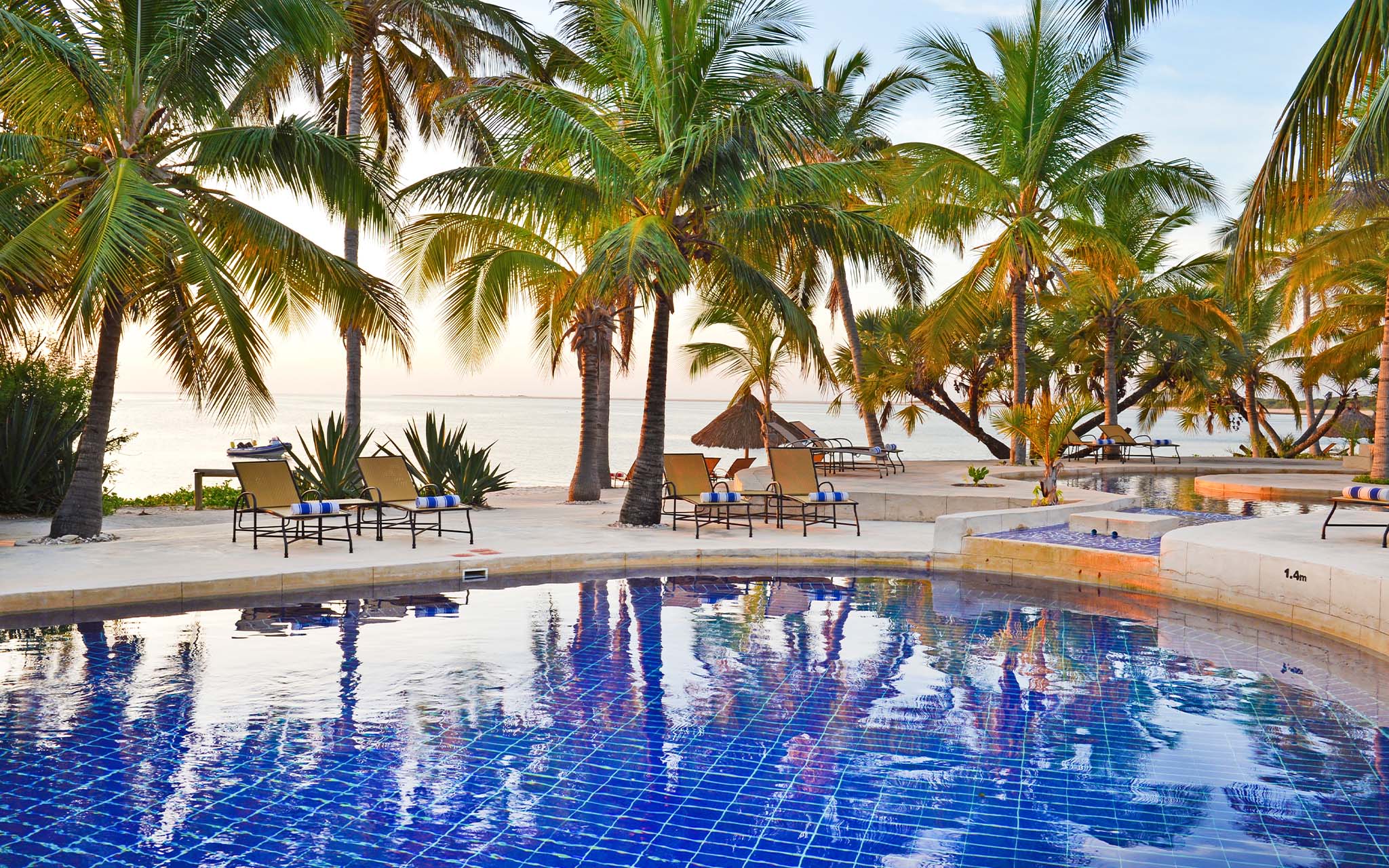 Piscina de Pestana Bazaruto Lodge, en Mozambique, rodeada de palmeras y tumbonas, con la playa enfrente