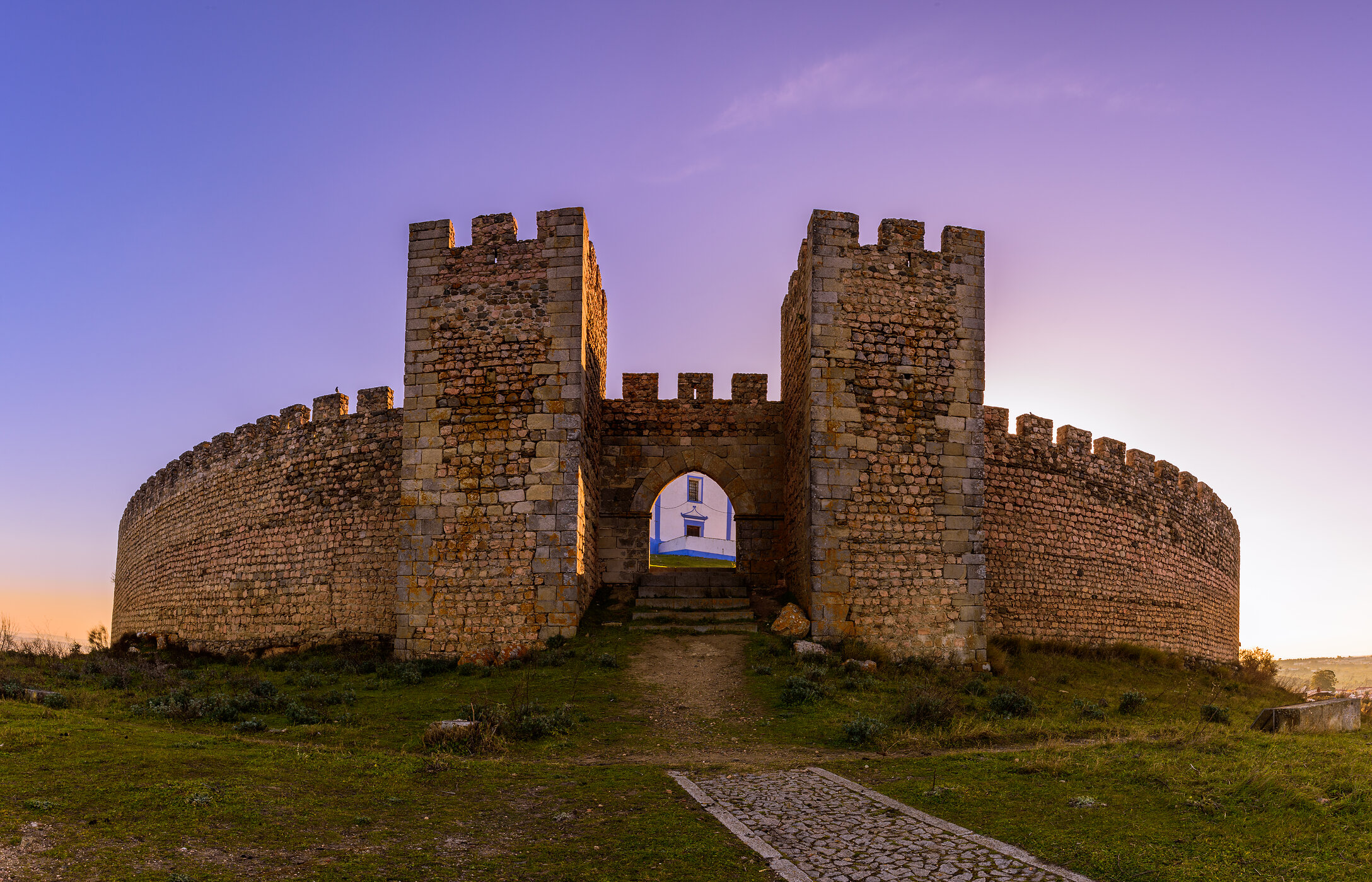 Vista frontal imponente de la entrada del castillo de Arraiolos, con muros de piedra y vegetación alrededor