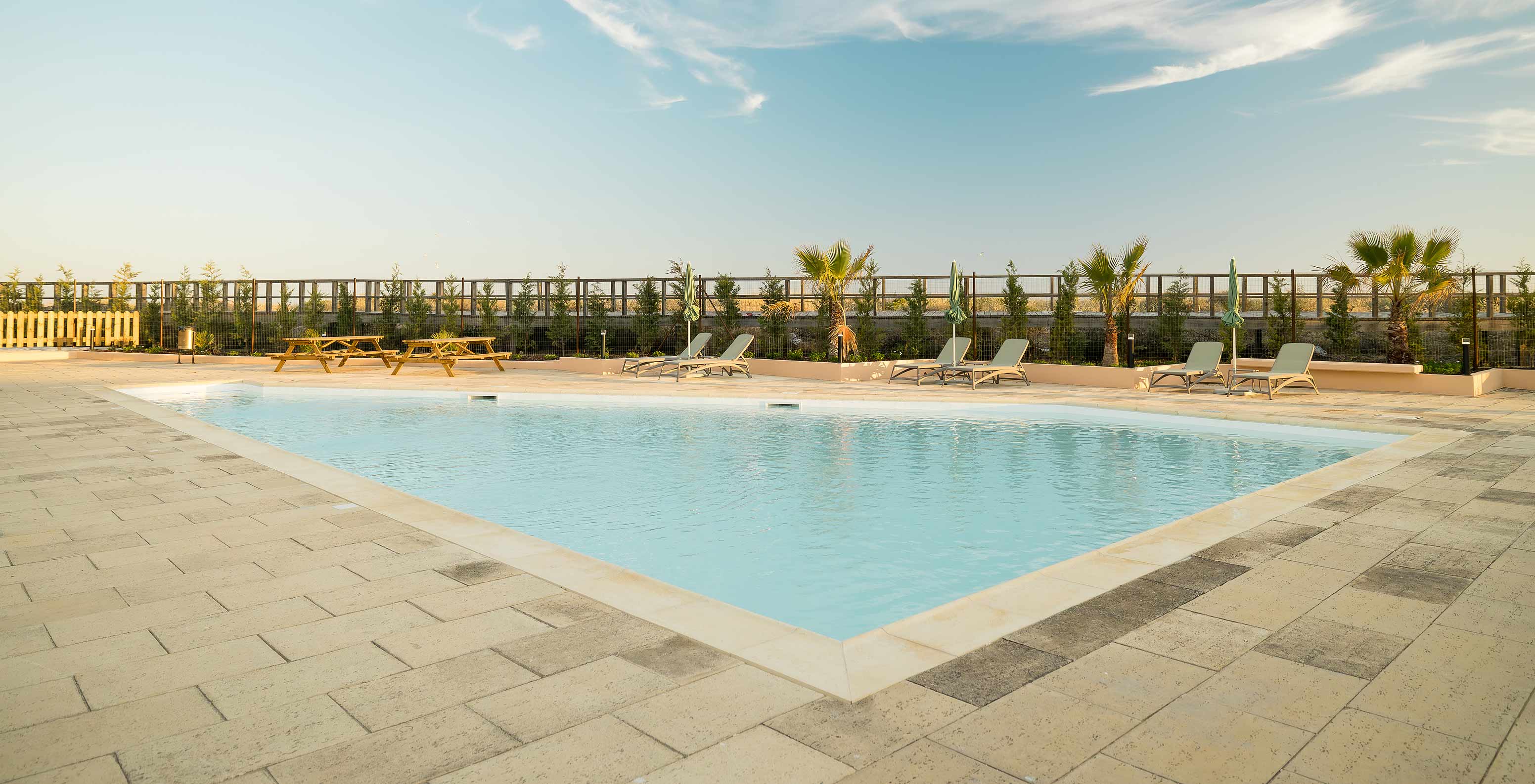 Piscina infantil del hotel cerca de la playa, varias tumbonas, palmeras y vista al sendero de acceso a la playa
