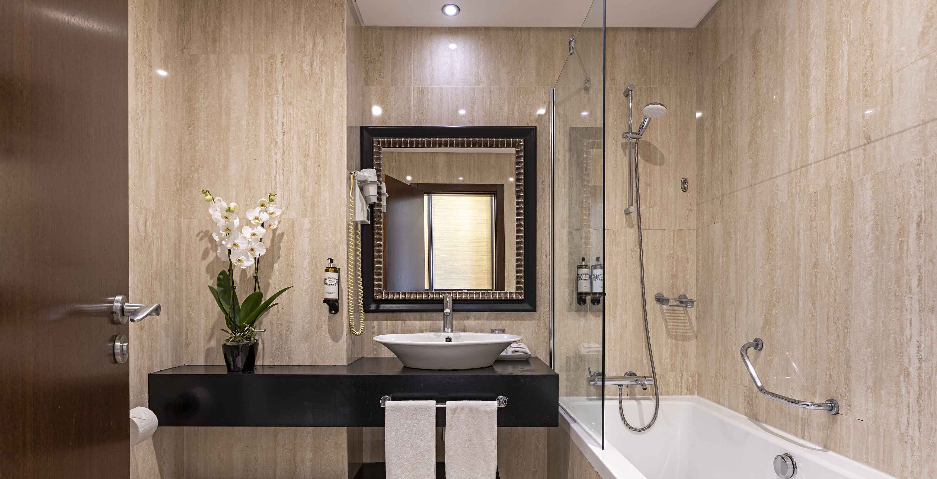 La Cliff Suite T2 en Pestana Alvor Praia tiene un baño moderno con una bañera, un lavabo, un inodoro, un espejo y flores