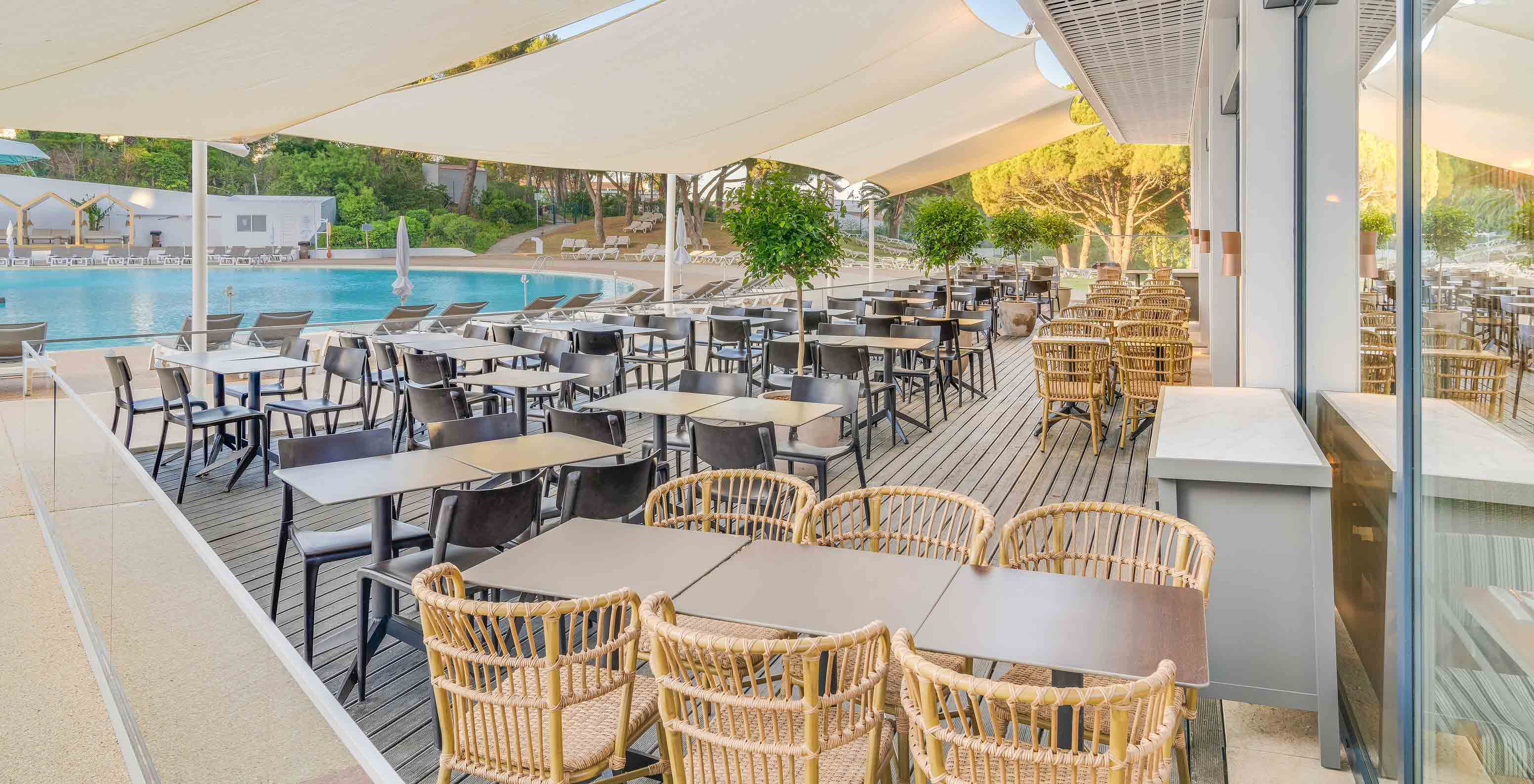 El bar Acqua, del Hotel Todo Incluido en el Algarve, tiene mesas y sillas en el exterior junto a la piscina.