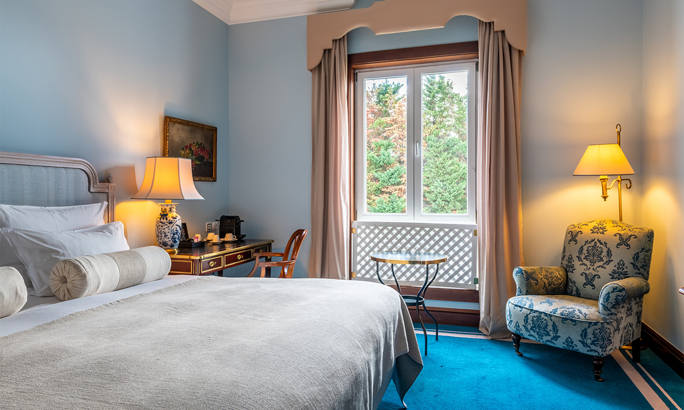 El Deluxe del Pestana Palace Lisboa tiene una cama, un escritorio, una ventana con reja decorativa y alfombra azul