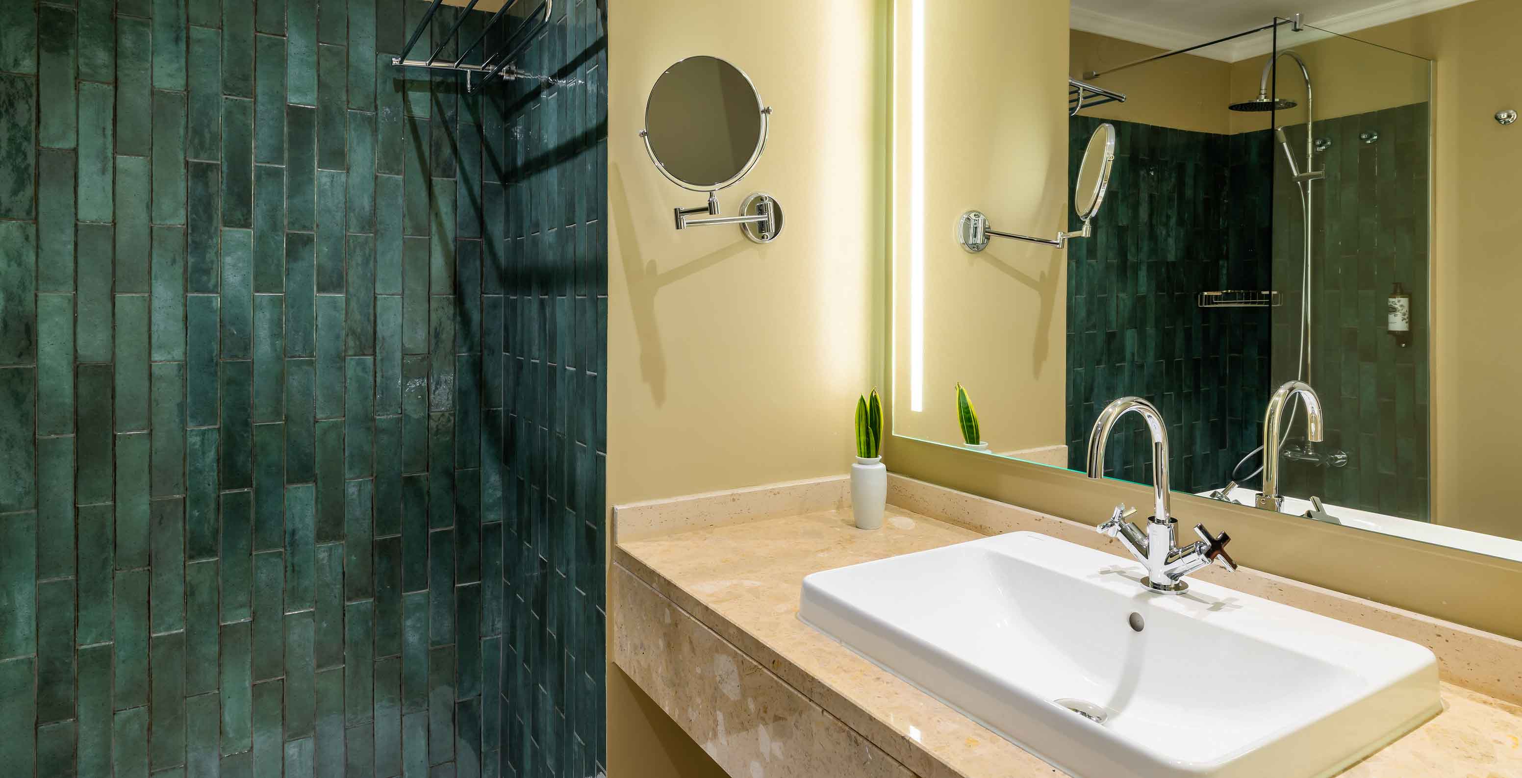 La Habitación Vista Piscina del Pestana Quinta Perestrello tiene un baño con lavabo, espejo y azulejos verdes.