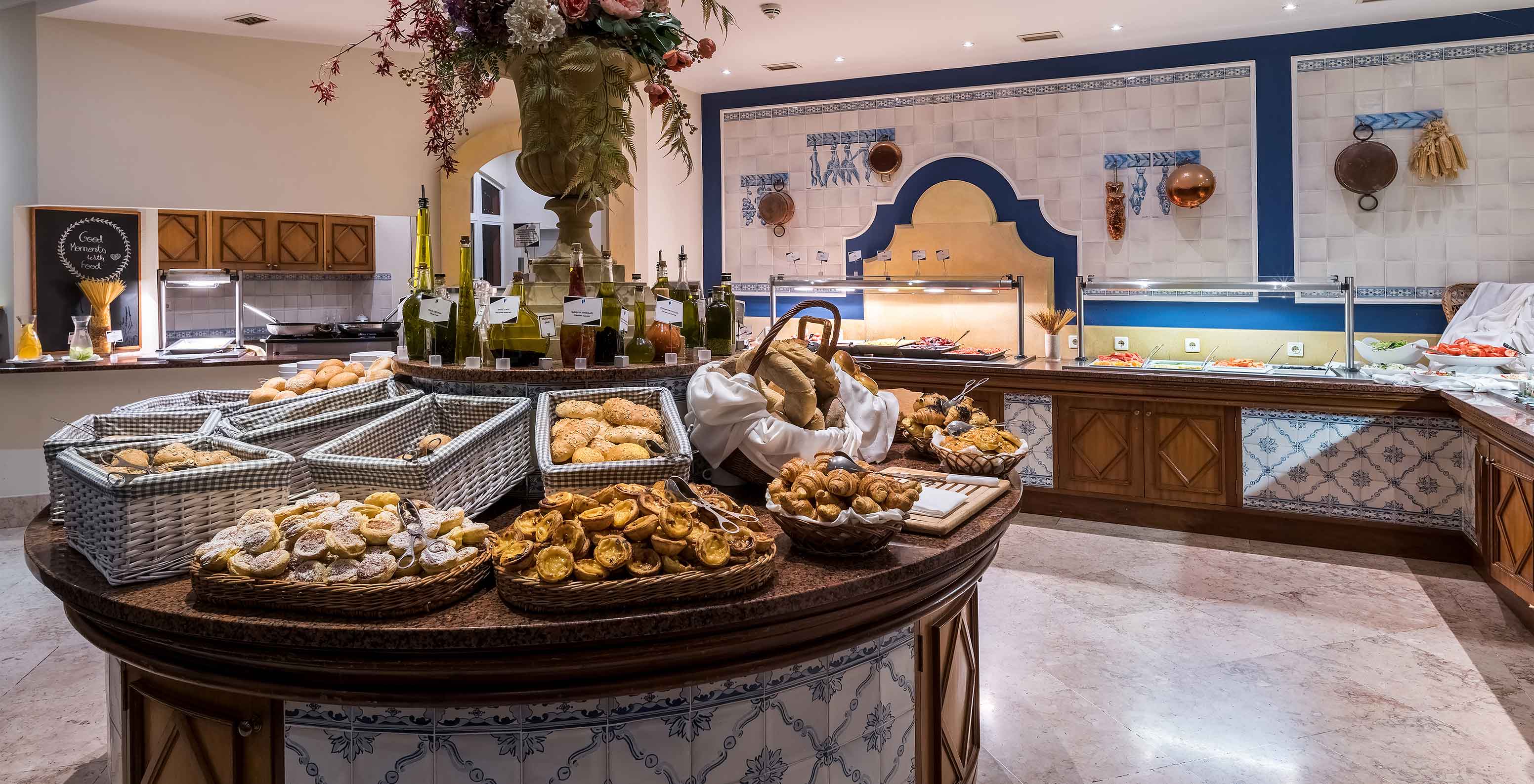 Sala de desayuno con varios panes y dulces en cestas sobre una mesa redonda del Pestana Village, Hotel con Piscina en Funchal