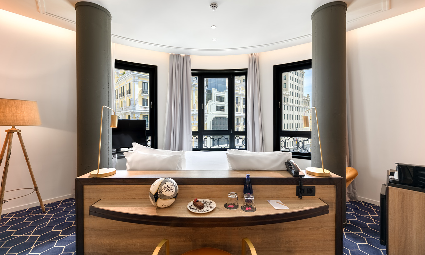 El Deluxe Grand con Vista del Pestana CR7 Gran Vía Madrid tiene una cama doble orientada hacia las ventanas en pared curva