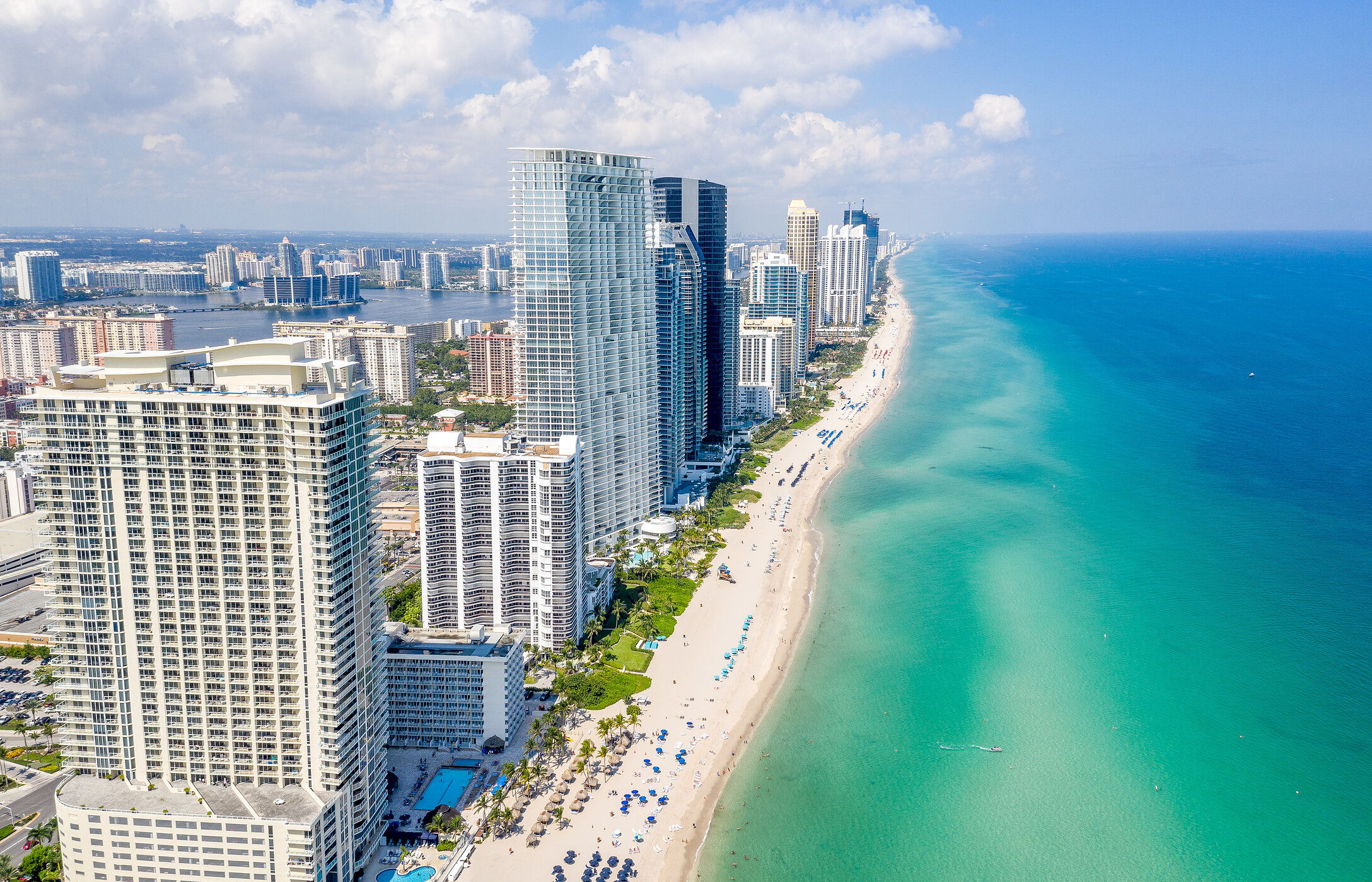 Vista aérea de la costa de Miami Beach, Florida, con una larga franja de arena blanca, agua cristalina y edificios altos.