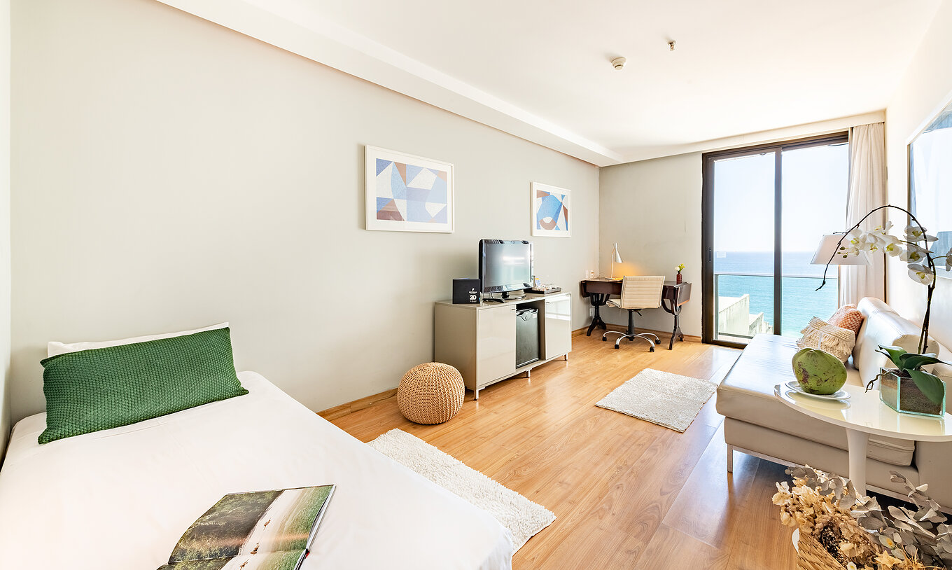 La Suite Vue Mer Latérale du Pestana Rio Atlântica a un salon avec canapé, télévision et fenêtre avec vue sur la mer