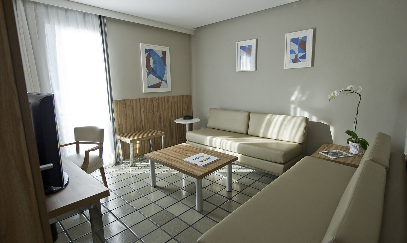La Suite du Pestana Rio Atlântica a un salon avec deux canapés beiges confortables, une table basse et une télévision