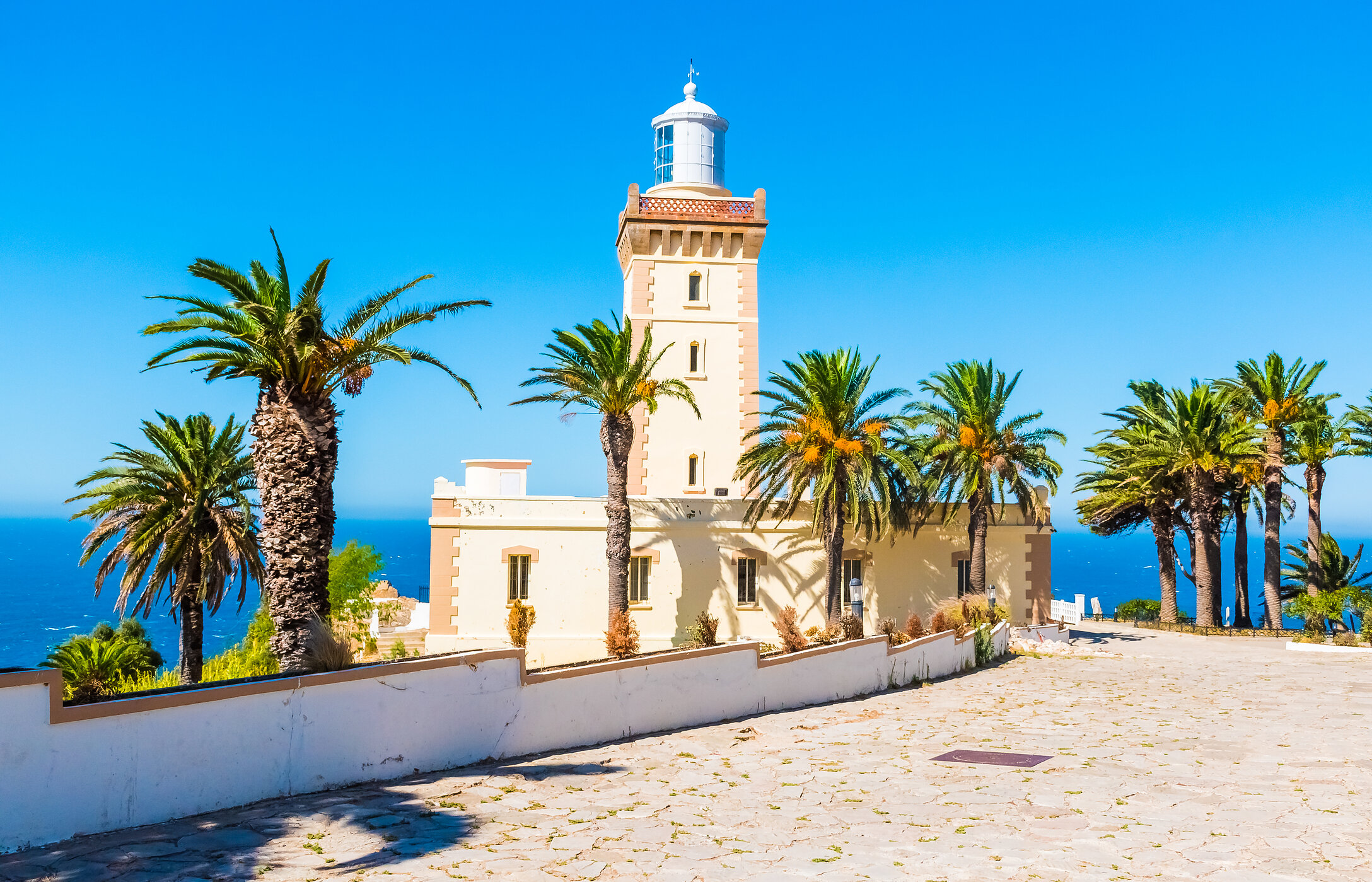 Le Cap Spartel, près de la ville de Tanger, a un phare blanc entouré de palmiers et de la mer devant