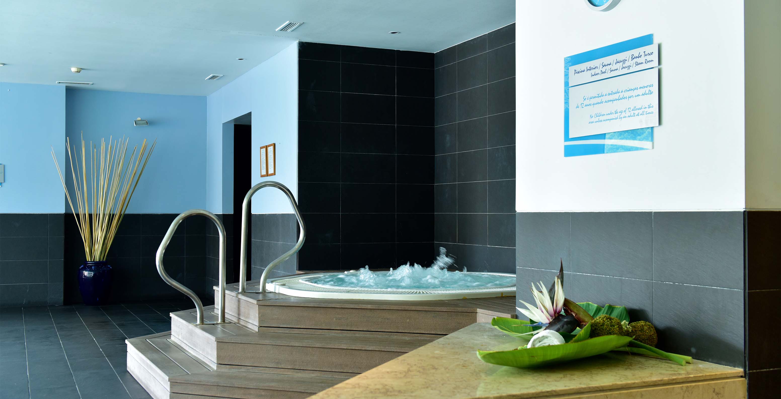 Jacuzzi avec échelles en bois et supports métalliques, avec sol en pierre noire et horloge murale