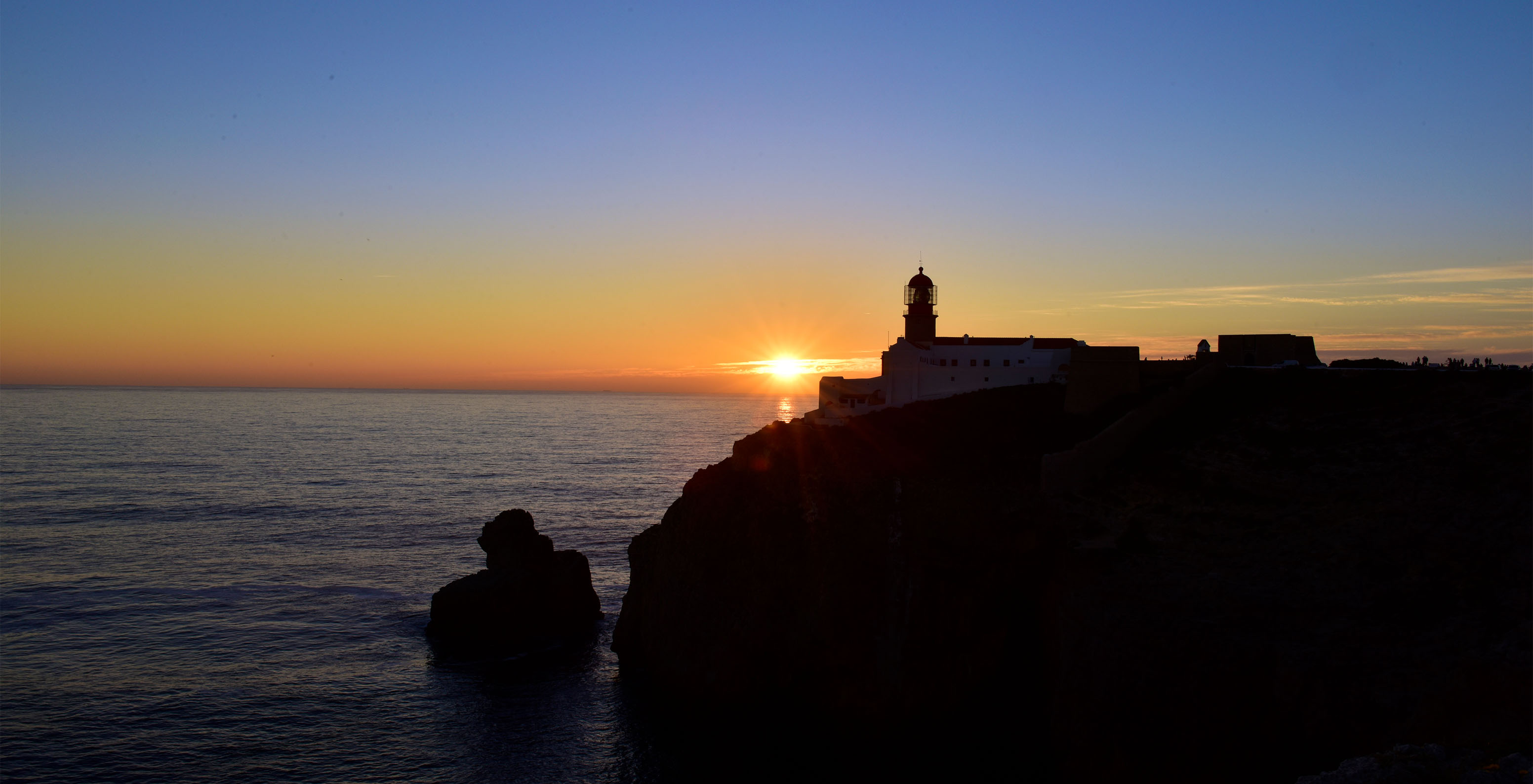 Coucher de soleil sur une falaise avec un horizon orange et un phare au sommet de la falaise