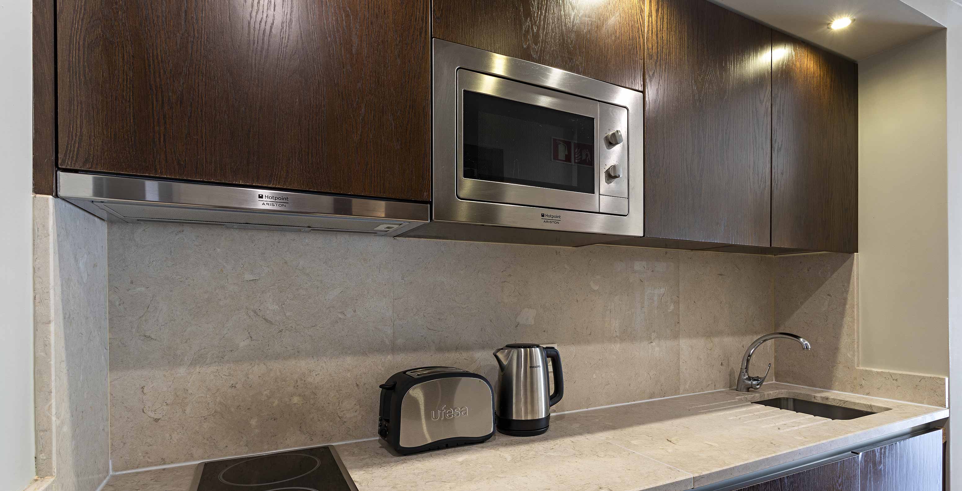 La Suite Cliff T1 du Pestana Alvor Praia a une cuisine en bois foncé, un plan de travail en pierre, plaques et micro-ondes